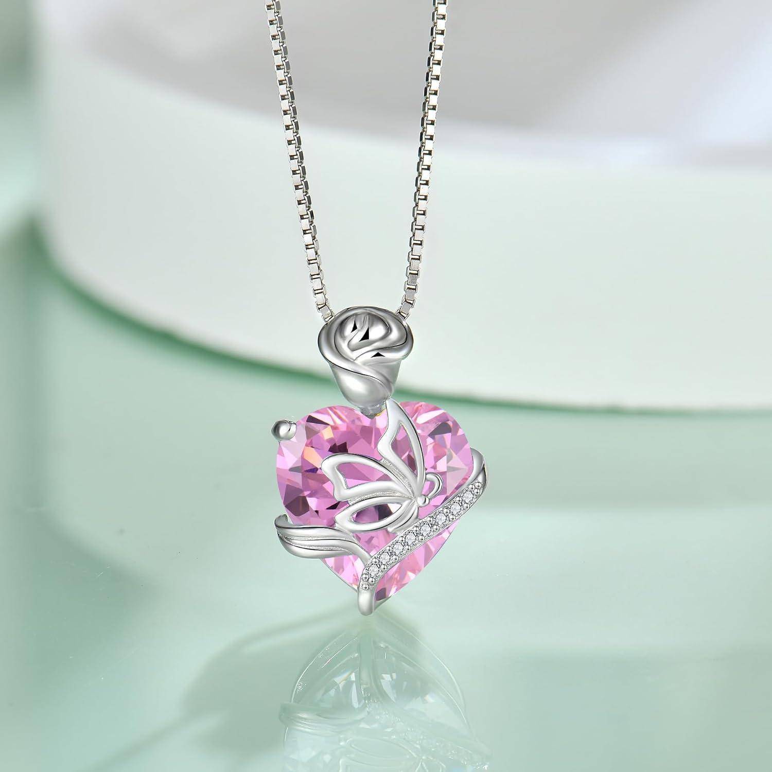 Silberanhänger-Halskette mit einem rosa facettierten herzförmigen Edelstein und Schmetterlingsdesign an einer Kette, vor einem weichen grünen Hintergrund dargestellt.