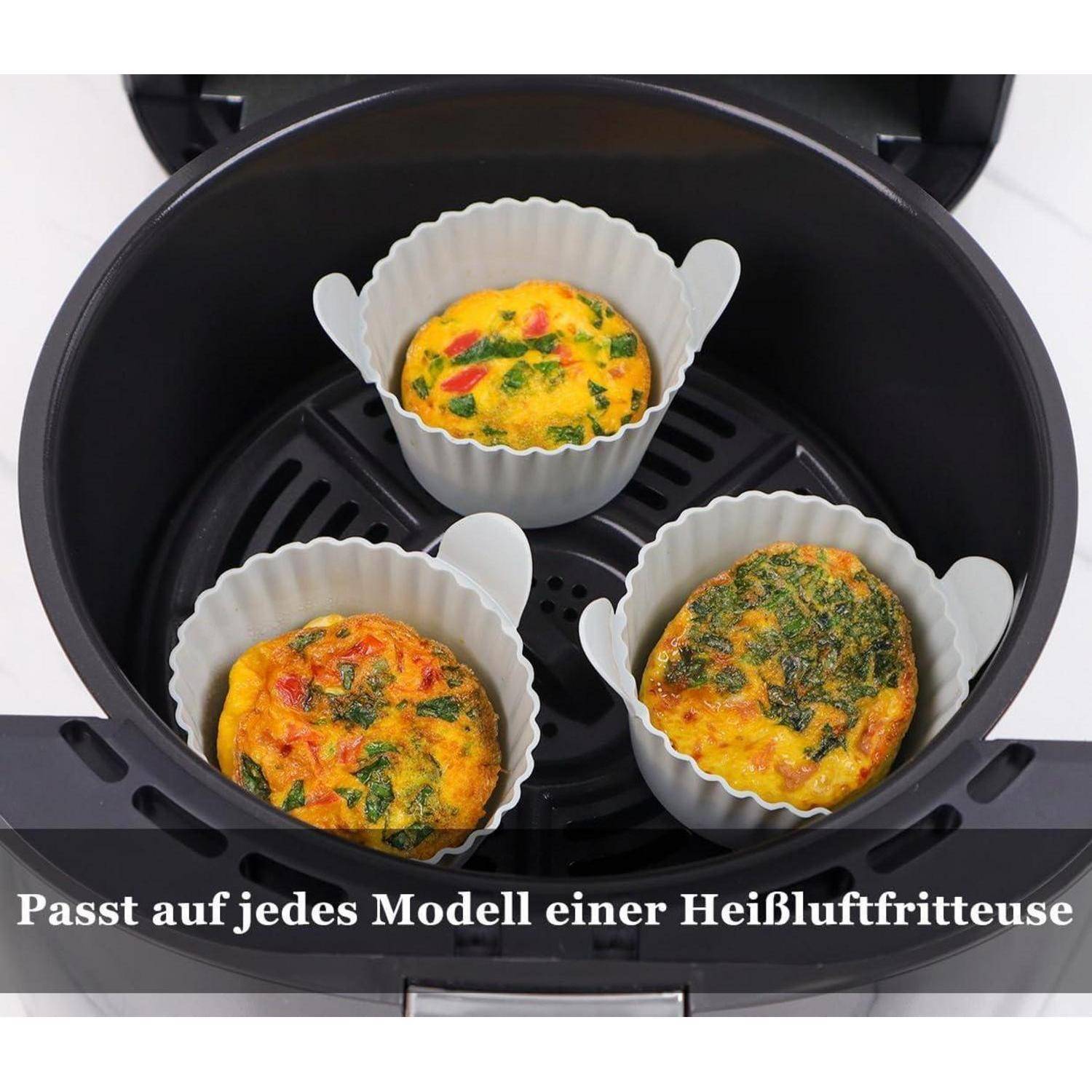 Drei Ei-Muffins in weißen Silikonförmchen in einem Heißluftfritteusenkorb, mit deutscher Textüberlagerung, die lautet „Passt auf jedes Modell einer Heißluftfritteuse