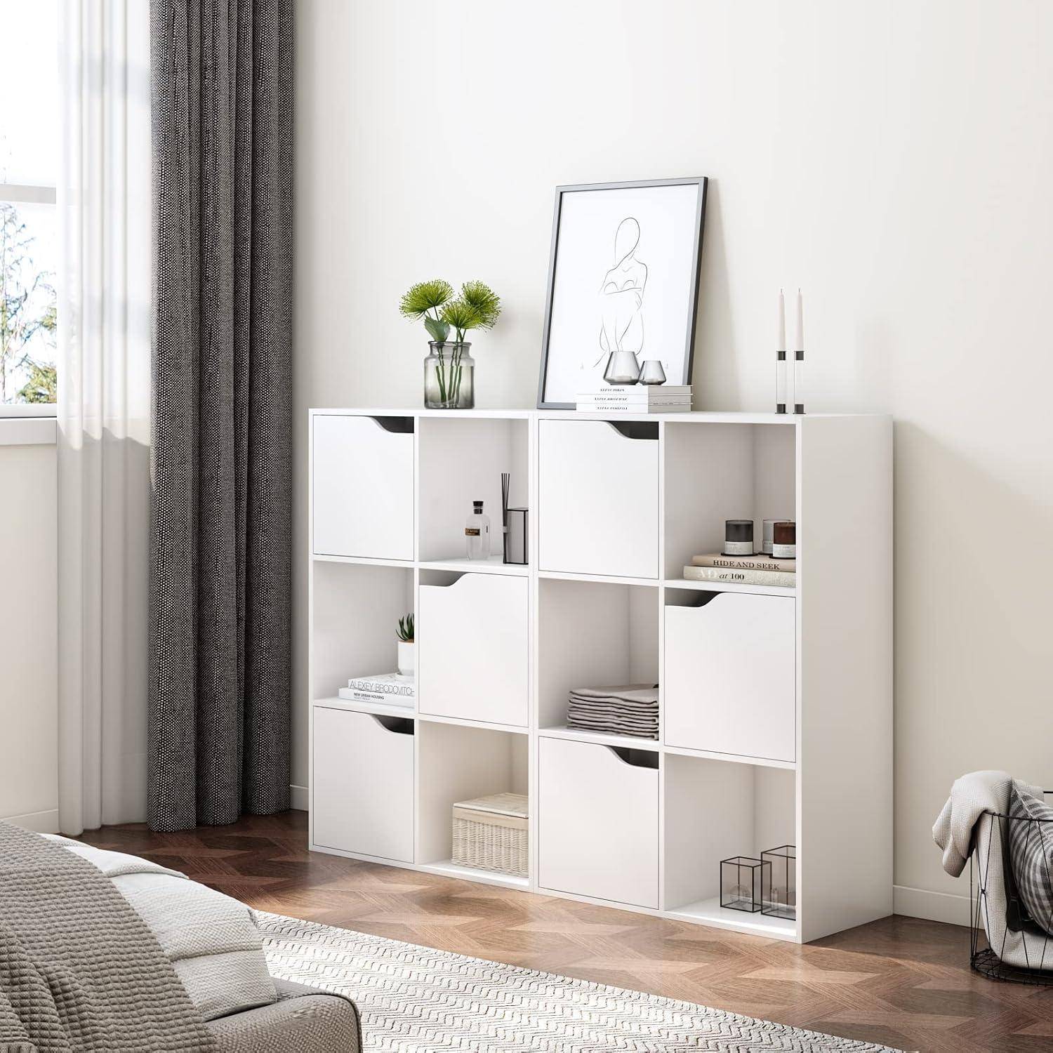 Modernes Wohnzimmer mit einer weißen würfelförmigen Aufbewahrungseinheit, die Bücher und Dekorationsgegenstände enthält, gerahmter Kunstwerke oben darauf, neben einem Fenster mit dunklen Vorhängen.