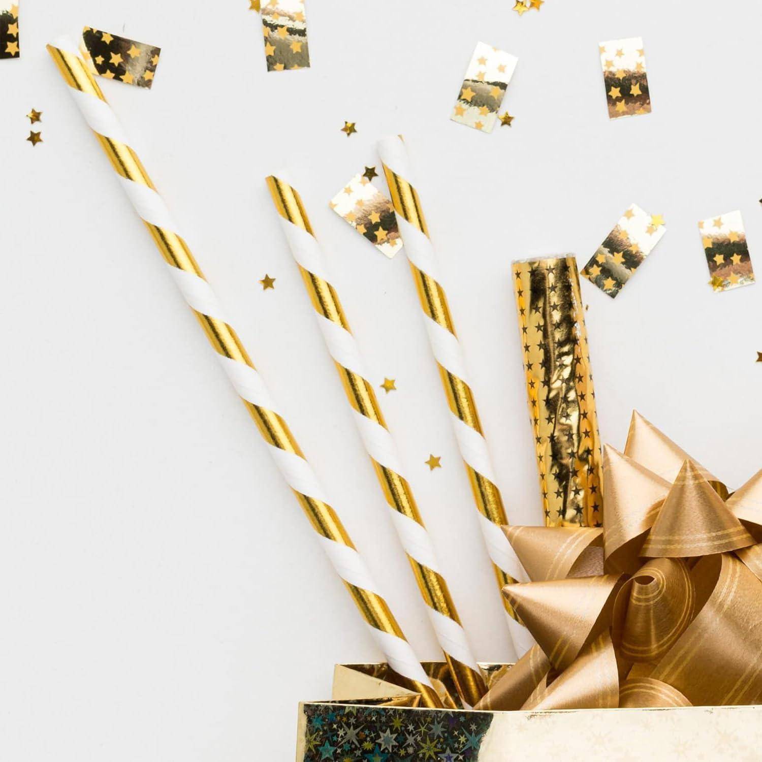Geschenktüte mit gold- und weiß gestreiften Papiertrinkhalmen, goldenem Sternkonfetti und einer metallisch goldenen Schleife auf weißem Hintergrund.