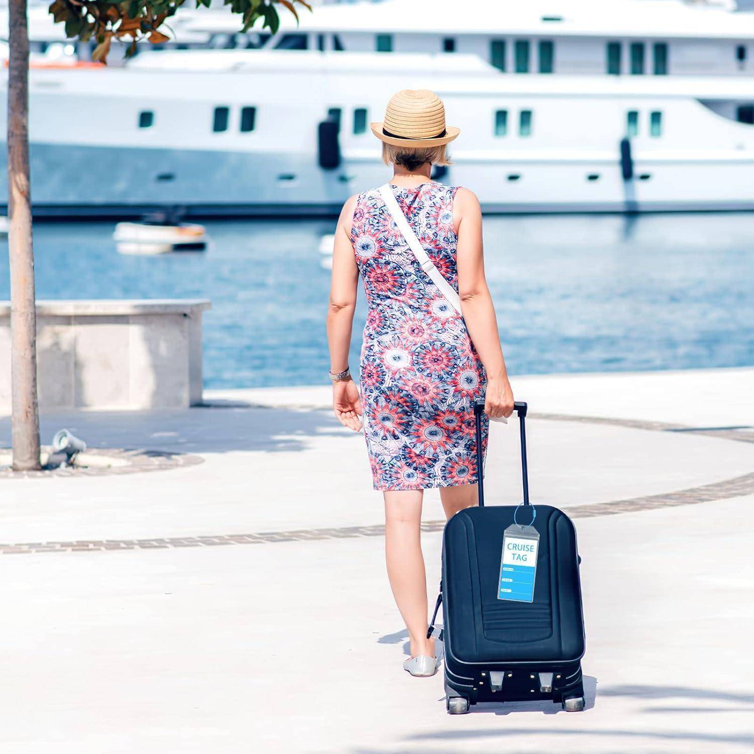 Frau in einem Blumenkleid und Strohhut zieht einen Koffer mit einem Kreuzfahrt-Etikett entlang eines Hafenstegs neben einem großen Schiff.