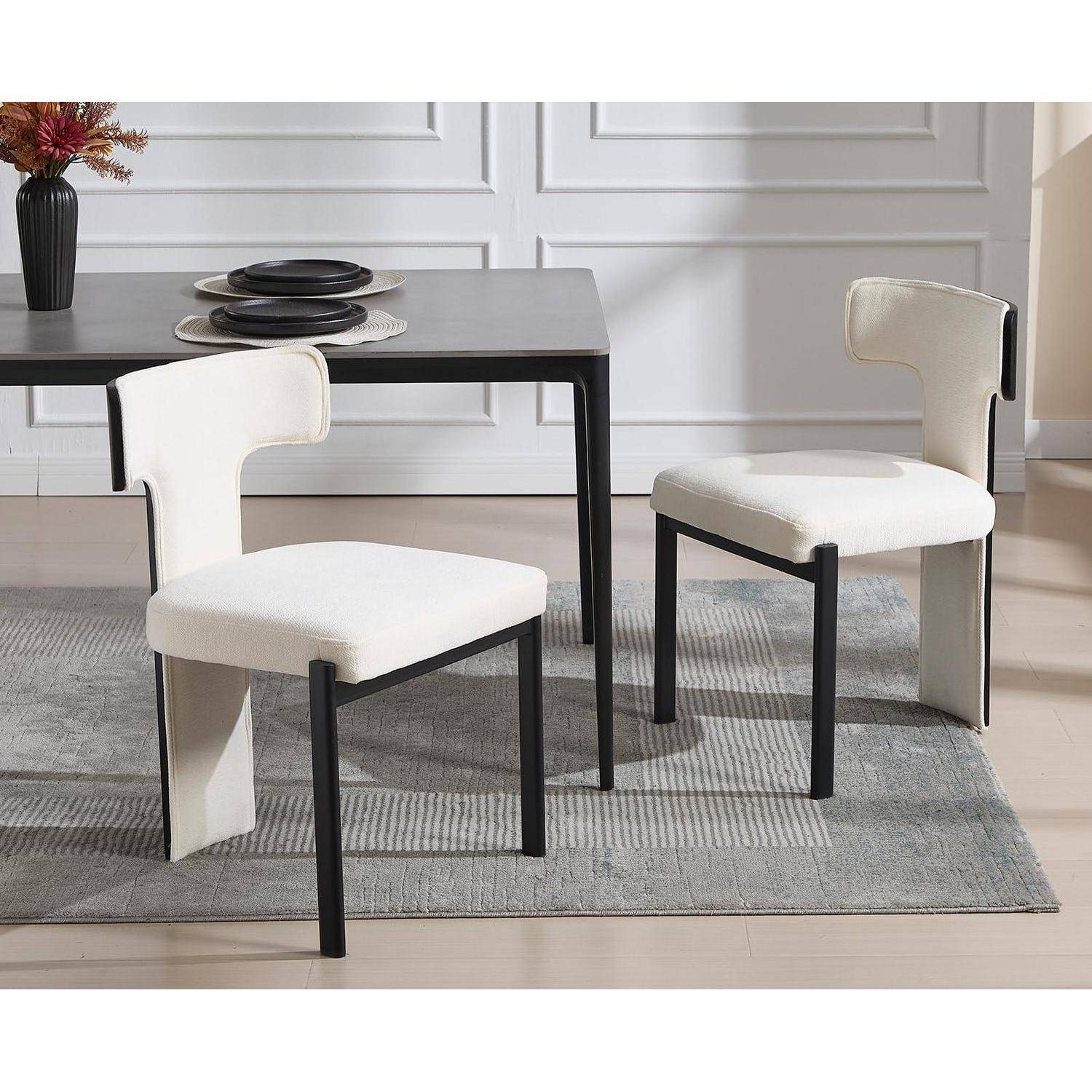 Modernes Esszimmerset mit schwarzem Tisch und zwei cremefarbenen gepolsterten Stühlen auf einem grauen Teppich in einem hellen Raum.