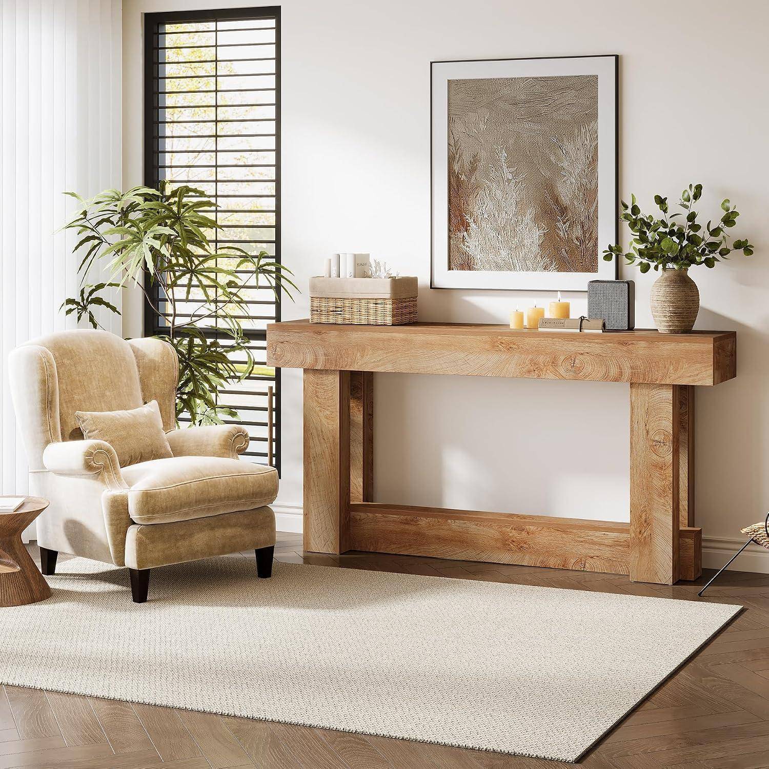 Gemütliches Wohnzimmer mit beigem Sessel, hölzernem Konsolentisch, eingerahmten Wandbildern, Pflanzen, Kerzen und großem cremefarbenem Teppich neben einem hellen Fenster.