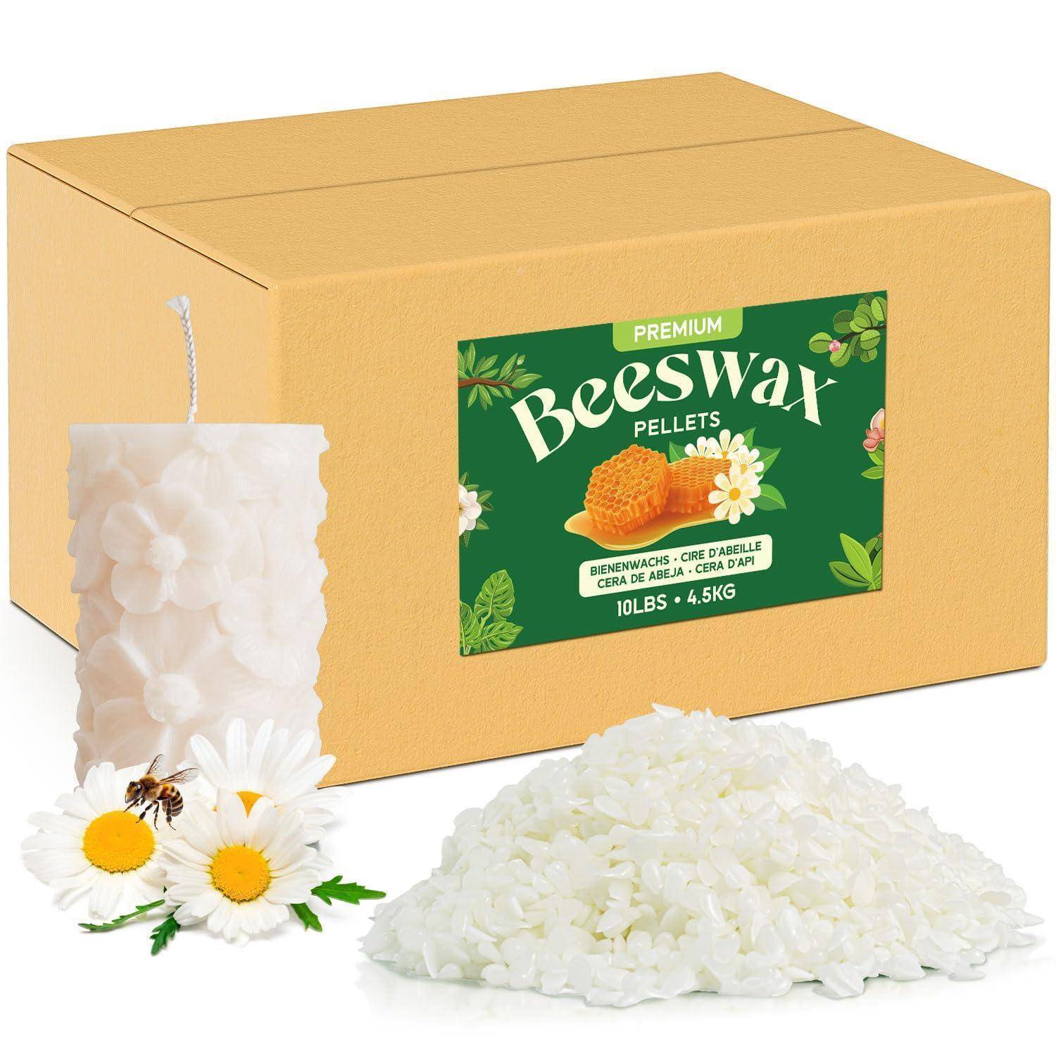 Schachtel mit Premium-Bienenwachspellets mit einer Bienenwachskerze, Gänseblümchenblüten und einem Haufen weißer Wachspellets auf weißem Hintergrund.