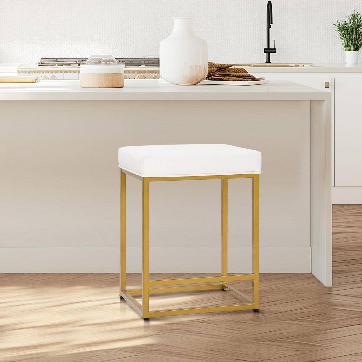 Barhocker mit goldfarmenem Rahmen und weißem gepolstertem Sitz in einer hellen modernen Küche mit weißer Insel und schwarzem Wasserhahn.
