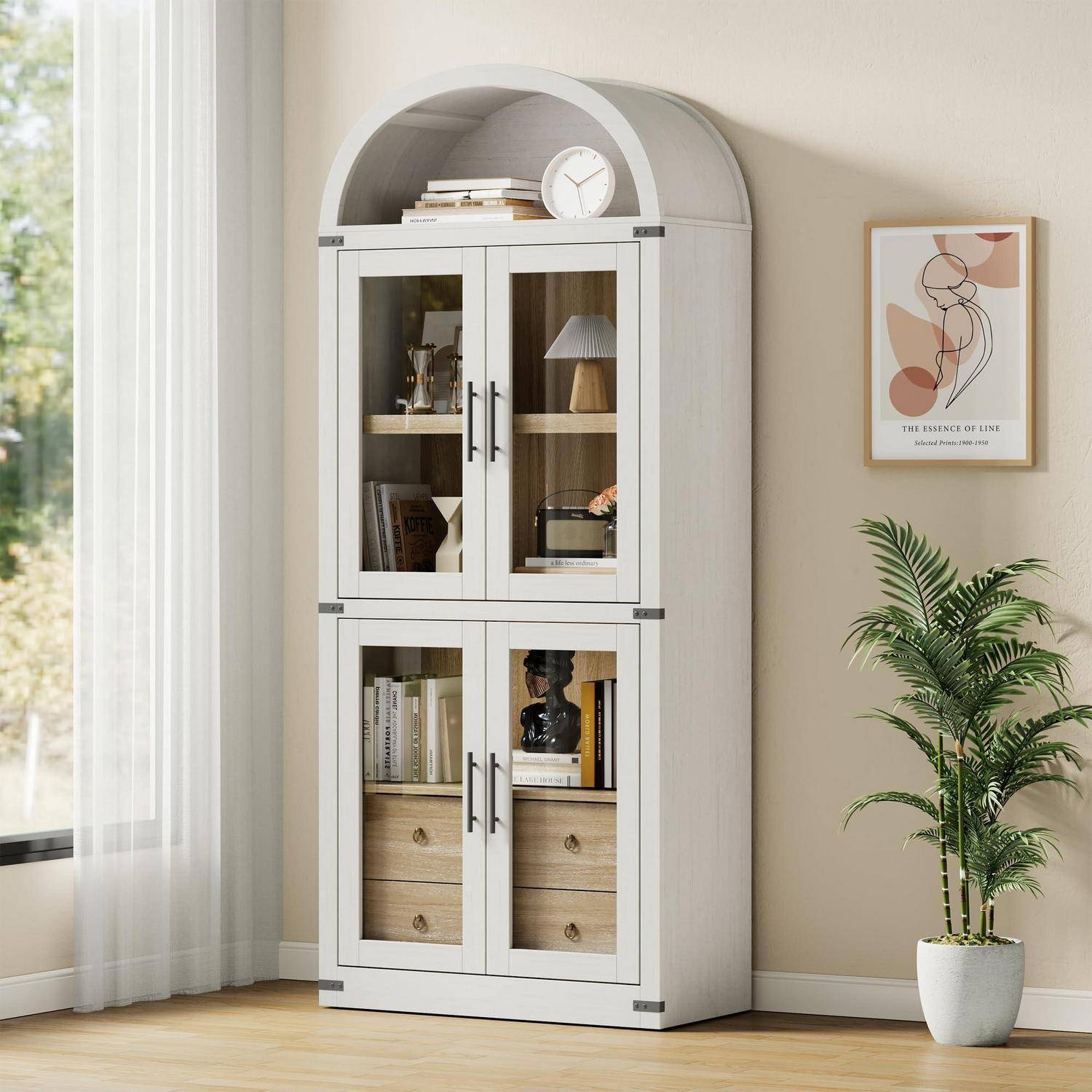 Weißer gewölbter Schrank mit Glastüren oben und Holzschubladen unten in einem hellen Raum, mit ausgestellten Büchern, Dekorationen und einer Lampe neben einer Topfpflanze.