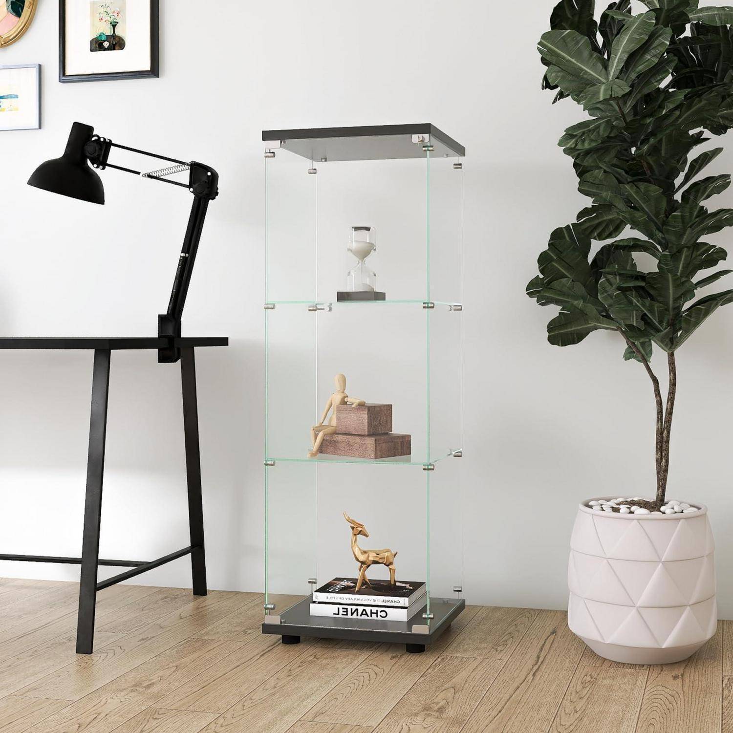 Modernes minimalistisches Zimmer mit einer schwarzen Schreibtischlampe, einem Glasvitrinnenschrank mit kleinen Dekorationsobjekten und einer großen Topfpflanze auf hellem Holzfußboden.