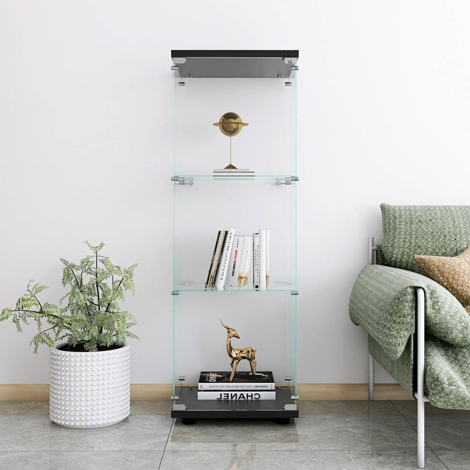 Ein Glaspräsentationsschrank mit dekorativen Objekten und Büchern steht neben einem grünen Sessel und einer Topfpflanze in einem minimalistischen Wohnzimmer.
