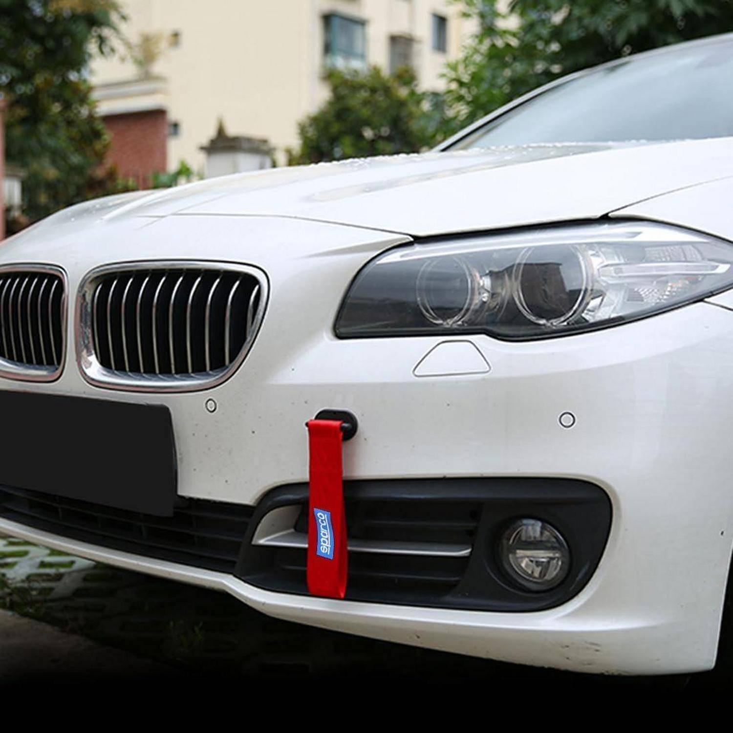 Vorderseite eines weißen BMW mit einem roten Abschleppstropp, der an der unteren Stoßstange befestigt ist, geparkt im Freien.