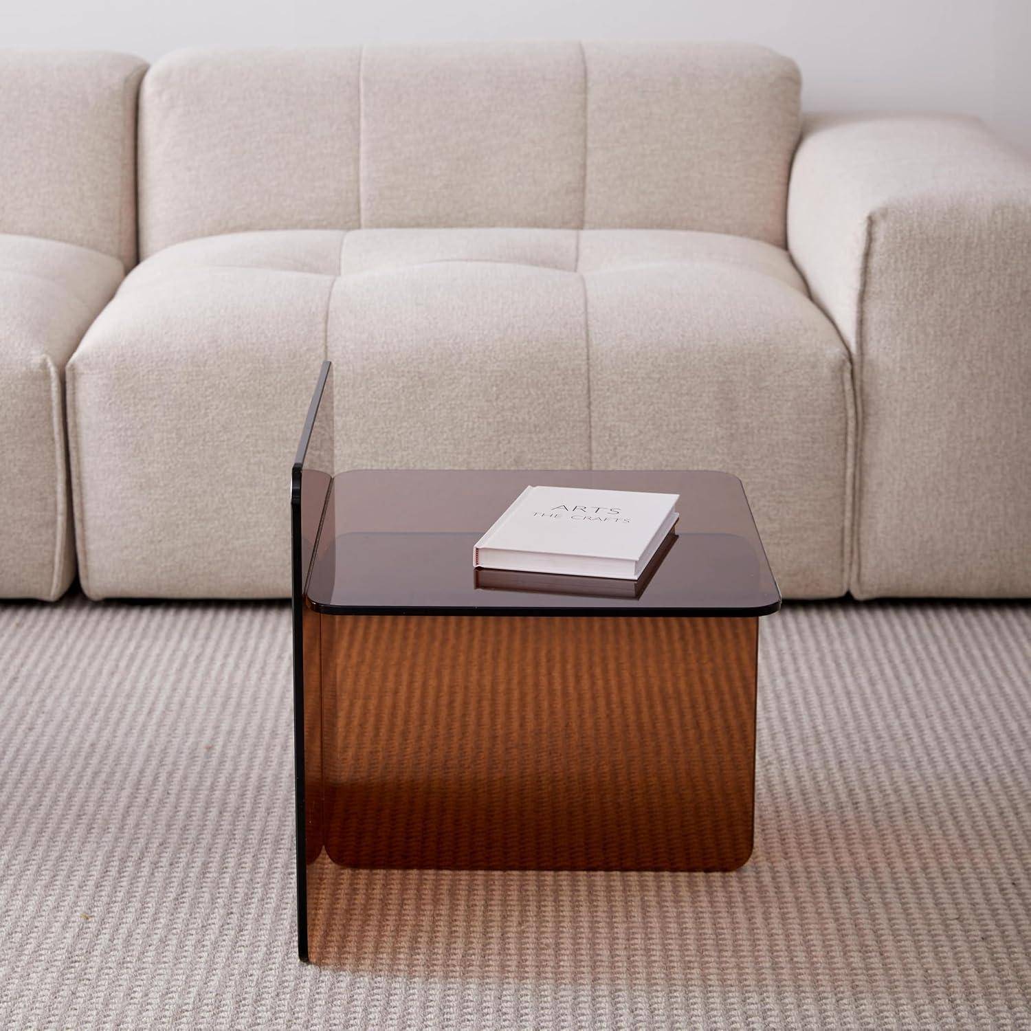 Modernes beiges Sofa hinter einem kleinen Beistelltisch aus Rauchrauchtglas auf einem gestreiften Teppich, mit einem weißen Buch oben drauf.