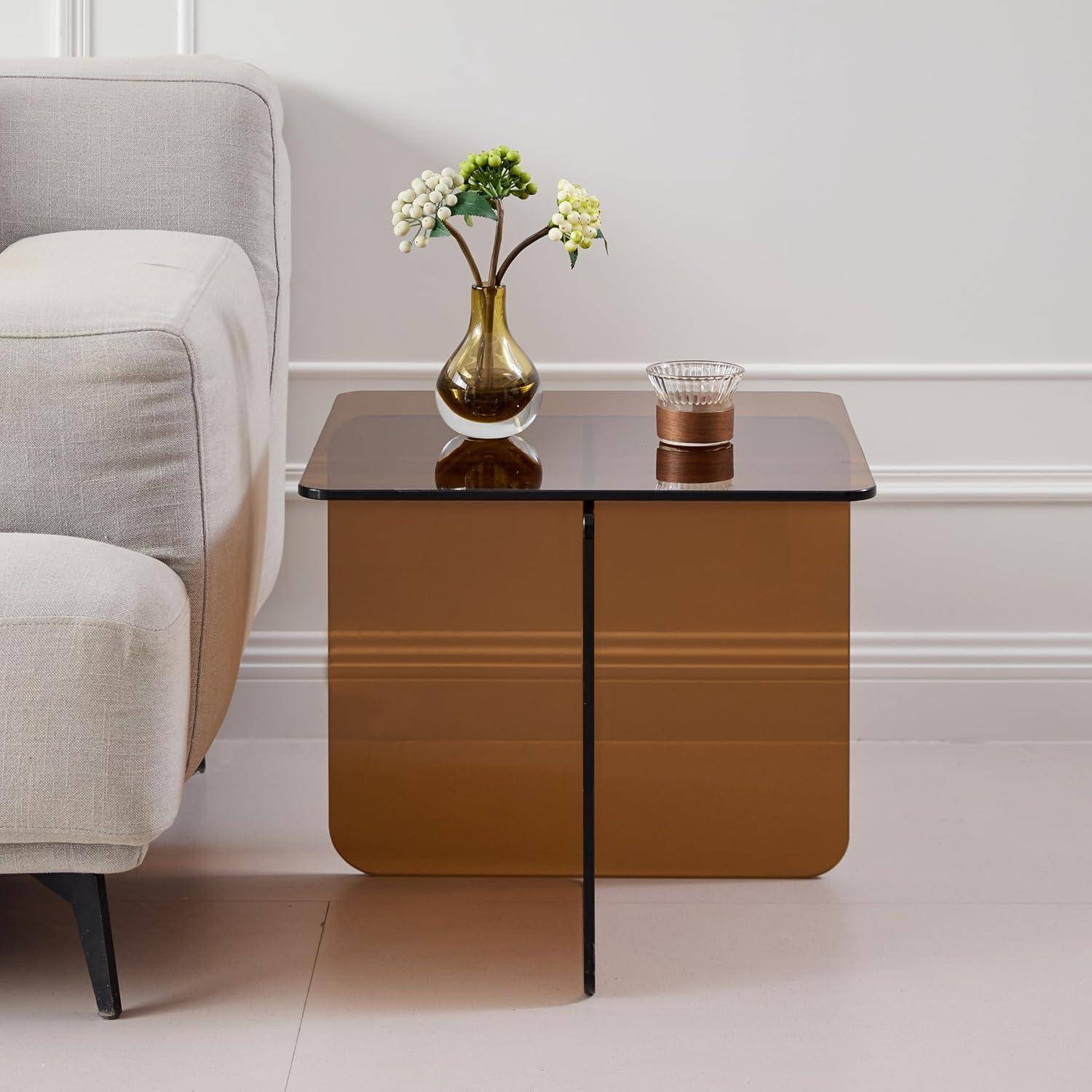 Moderner Beistelltisch aus Bronze mit Glasplatte neben einem beigen Sofa, auf dem eine kleine Blumenvase und ein Kerzenhalter stehen.