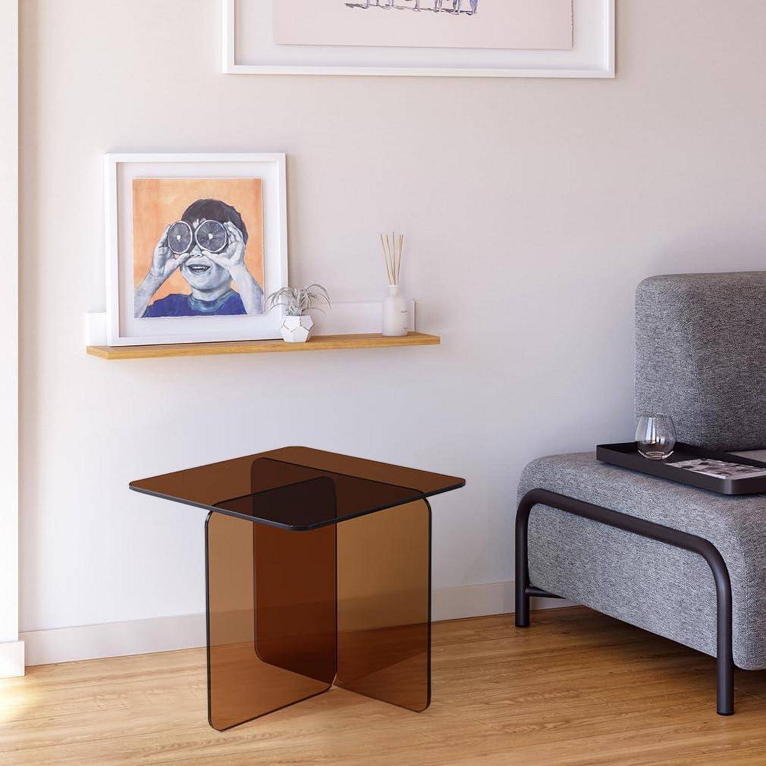 Modernes Wohnzimmer mit Bernsteinglas-Beistelltisch, grauem Sessel, schwebendem Regal mit Bilderrahmen und hellem Holzboden.
