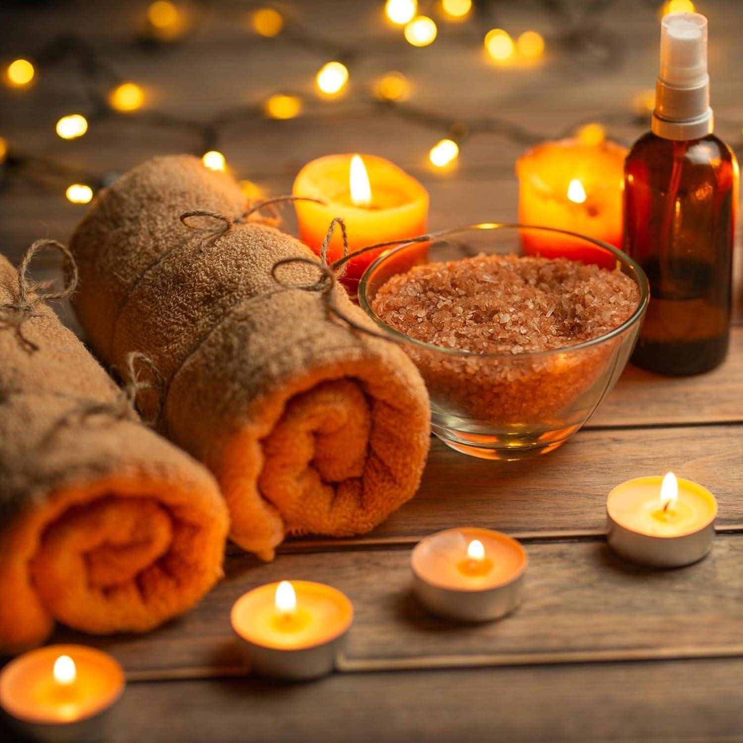 Spa-Szenerie mit gerollten orangefarbenen Handtüchern, brennenden Kerzen, einer Schüssel mit Badesalz und einer Sprühflasche auf einer Holzoberfläche.