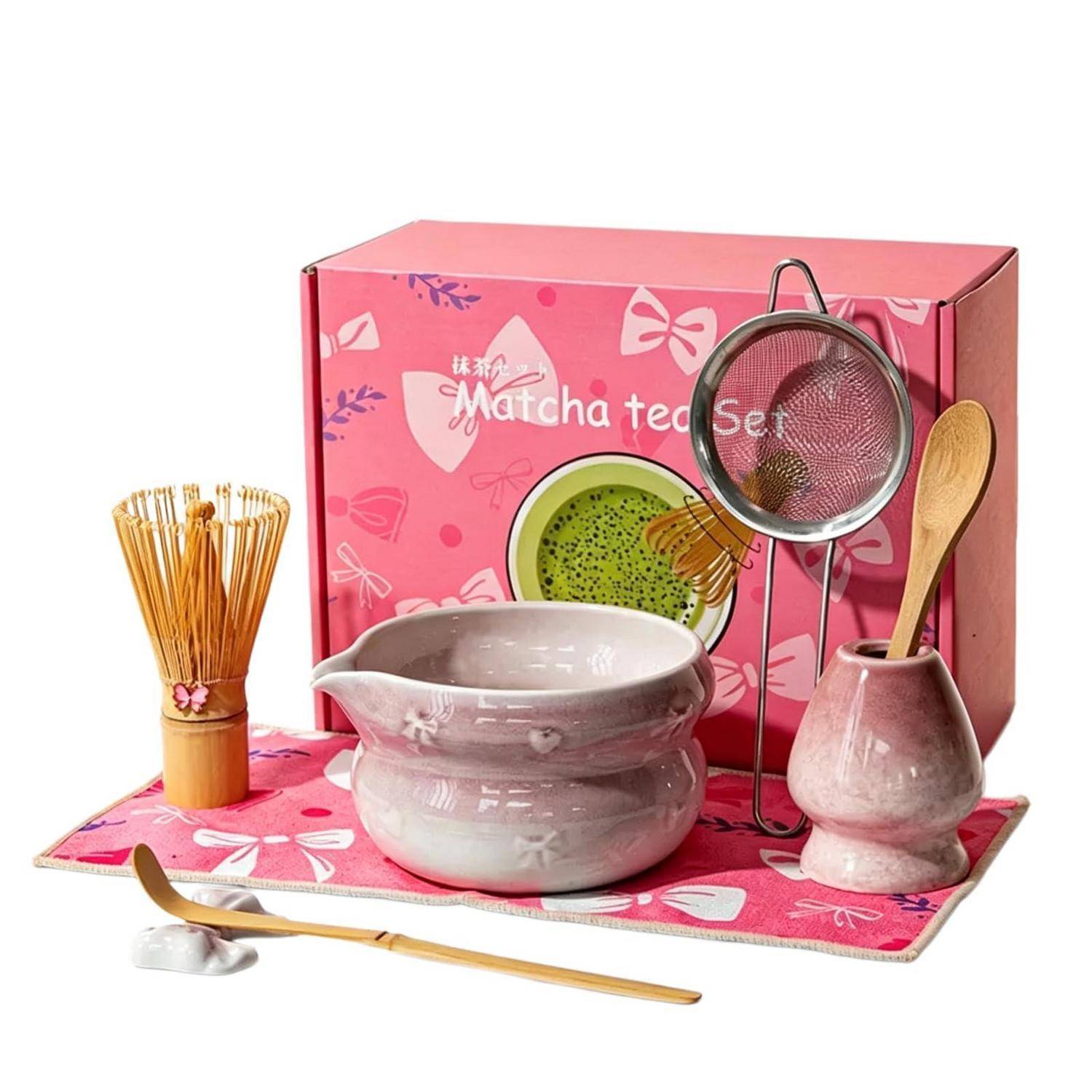 Matcha-Tee-Set Geschenkbox mit Schüssel, Besen, Sieb, Löffel, Besenhalter und Bambusbesen auf einer rosa Matte.