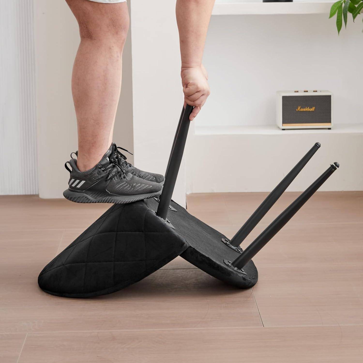 Person in Sneakers kippt einen schwarz gepolsterten Stuhl kopfüber um, während er auf dessen Sitz steht, wobei Möbel auf einem Holzboden umgeworfen werden.
