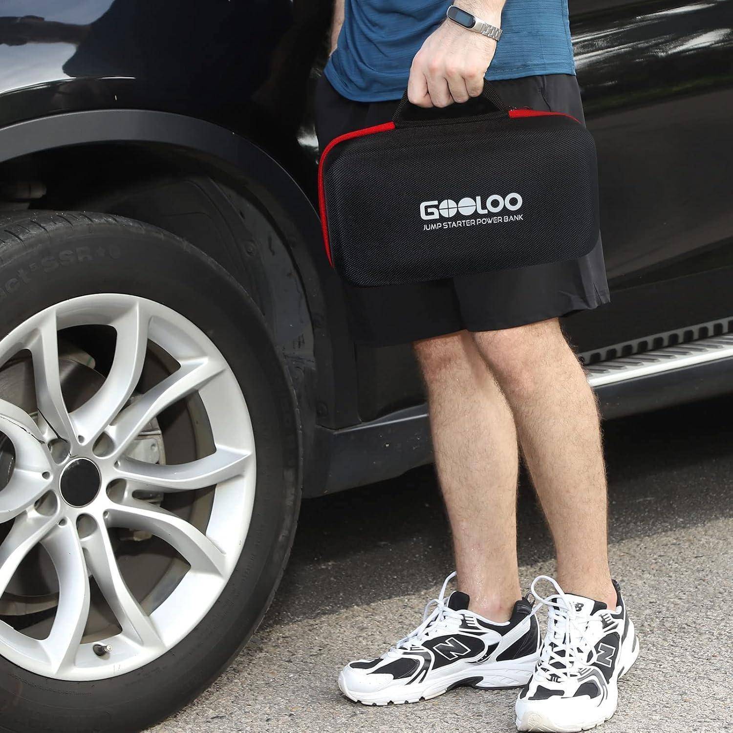 Person steht neben einem Auto und hält ein GOOLOO-Starthilfegerät-Powerbank-Etui in der Nähe des Vorderrades.