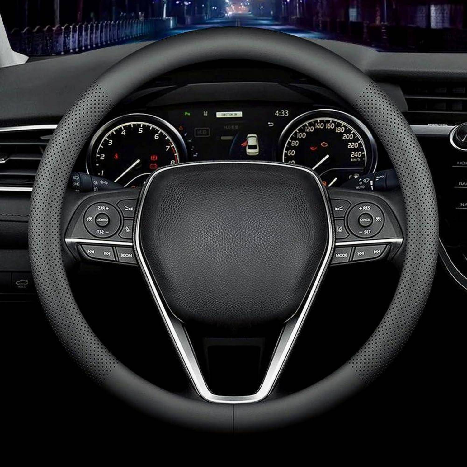 Nahaufnahme eines Autolenkrads und Armaturenbretts mit beleuchteten Instrumenten und einem kleinen Fahrerassistenz-Display.