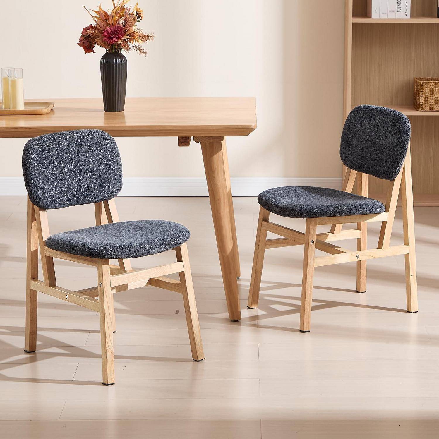 Zwei dunkelgrau gepolsterte Holzstühle neben einem Esstisch aus hellem Holz in einem hellen, minimalistischen Raum.