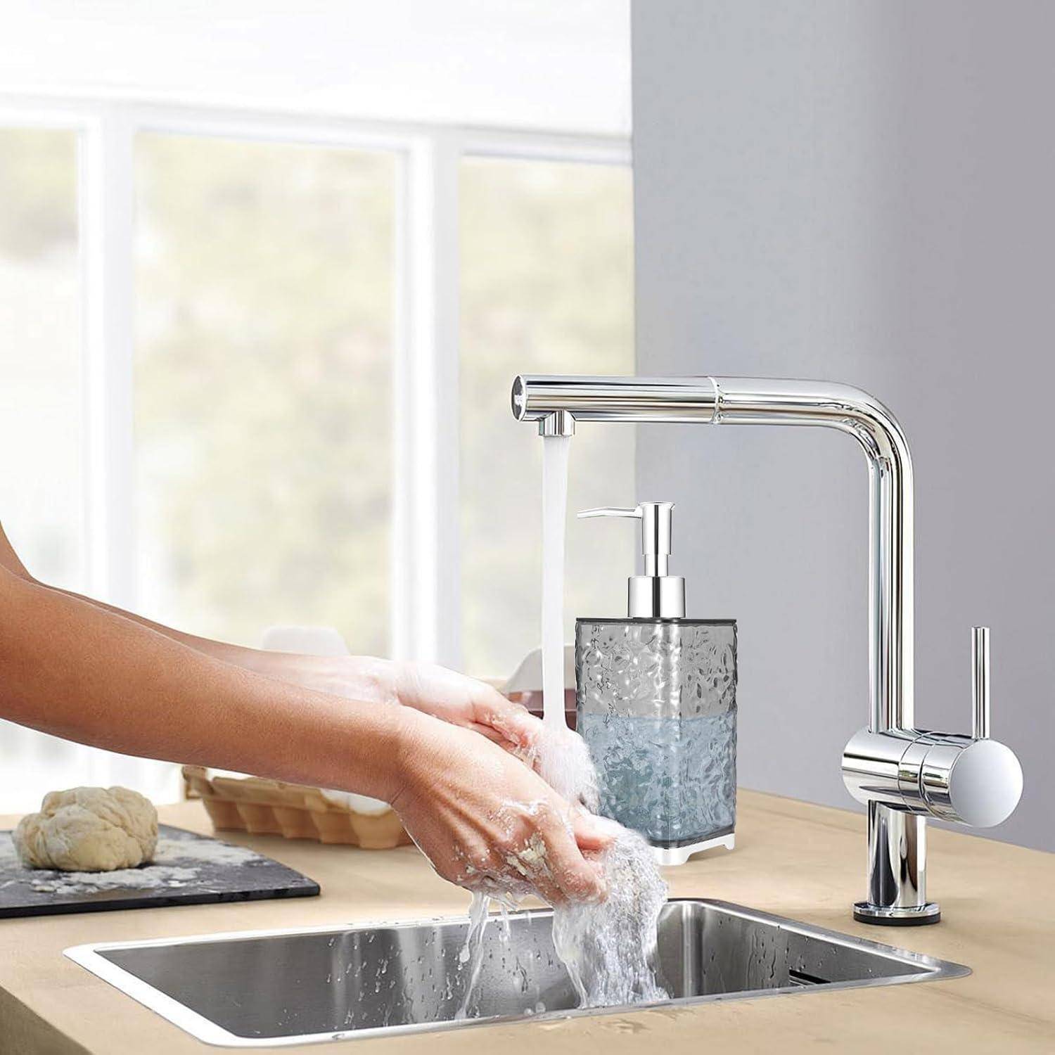 Hände werden unter einem laufenden Wasserhahn in der Küche neben einem Waschbecken gewaschen, mit einem Seifenspender und einem Reinigungsschwamm auf der Arbeitsplatte.