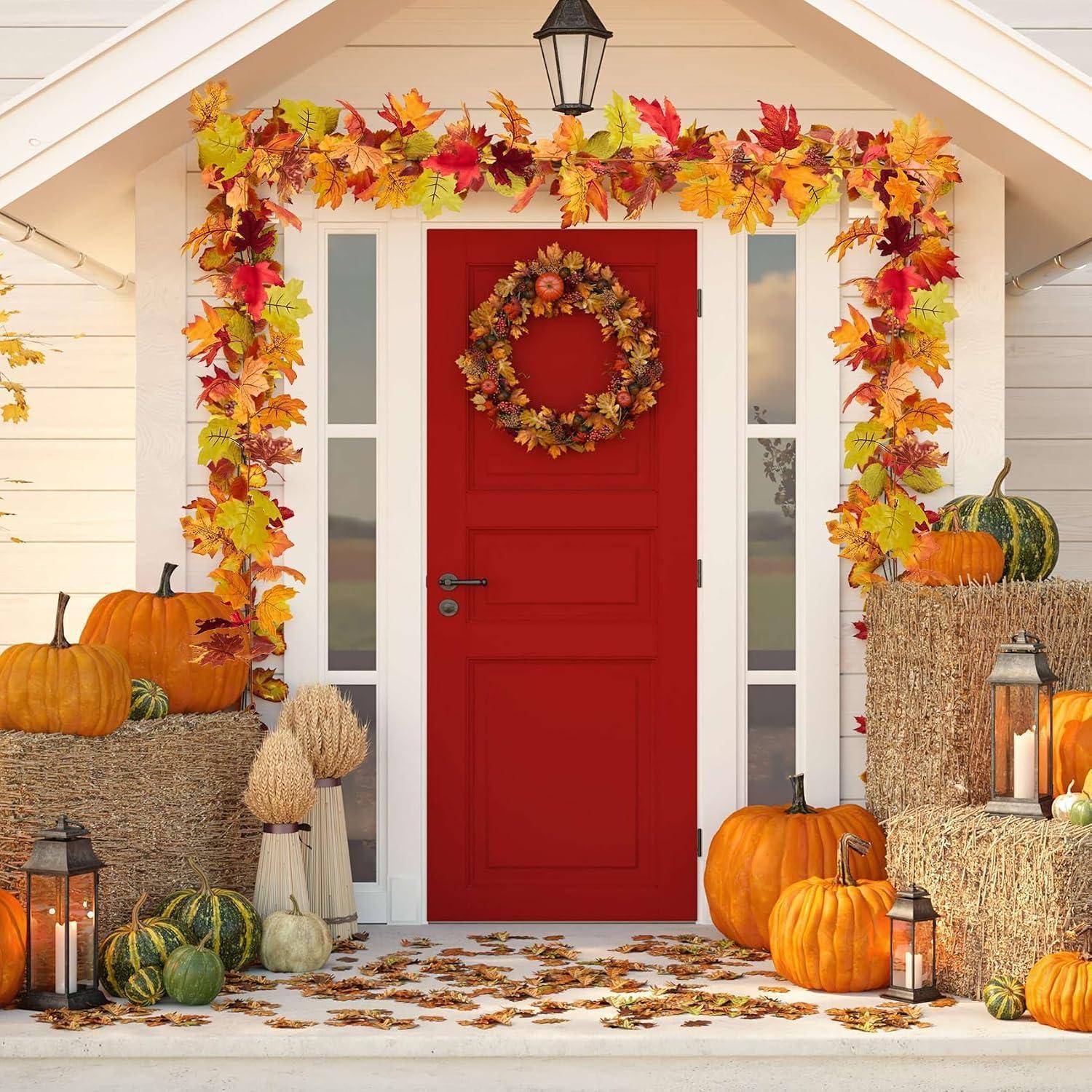 Rote Eingangstür, dekoriert mit einem Herbstkranz und einer Girlande, flankiert von Kürbissen, Heuballen, Laternen und Herbstblättern auf der Veranda.