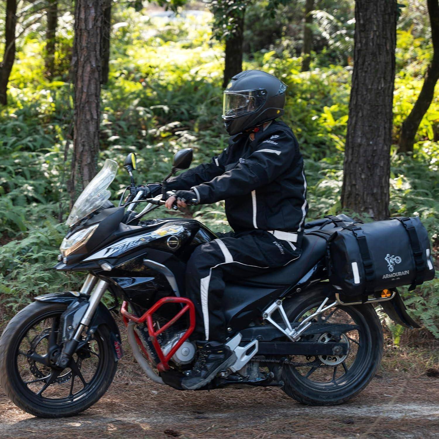 Motorradfahrer in schwarzer Schutzkleidung und Helm auf einem beladenen Touring-Motorrad auf einem Waldpfad.