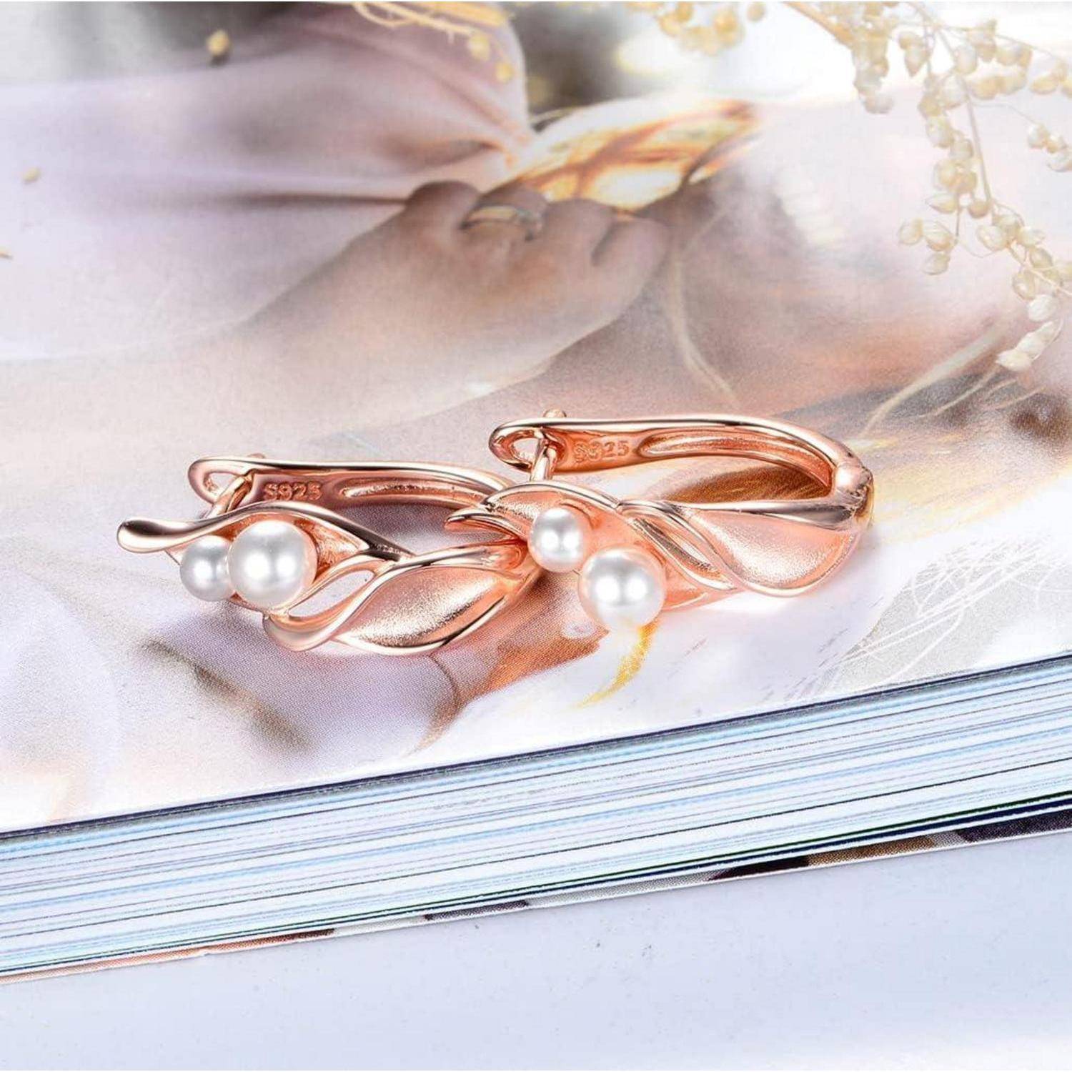Roségoldfarbene Perlenohrringe mit einem eleganten Blattdesign ruhen auf einer offenen Magazinseite.