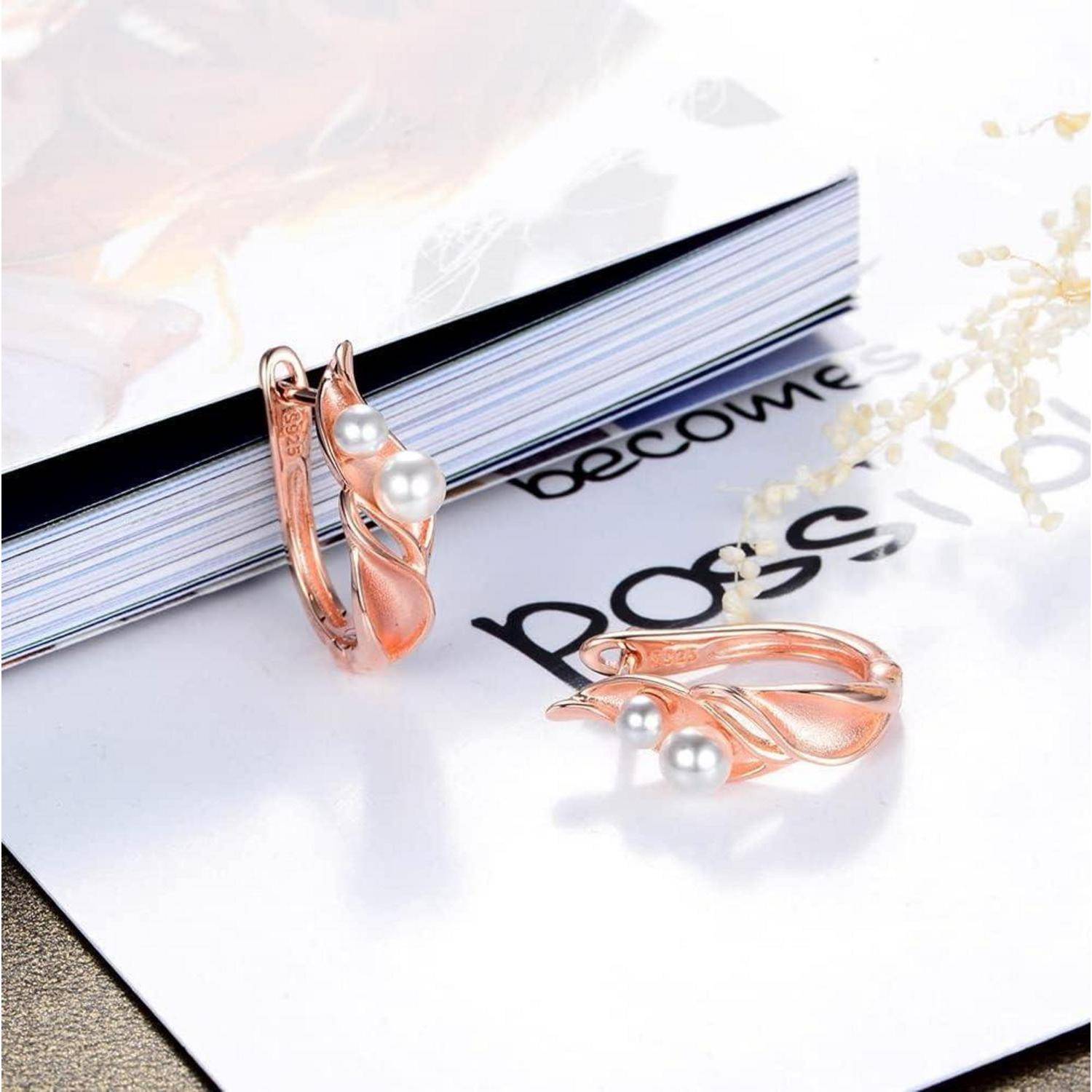 Ohrringe aus Roségold mit Perlen, die auf einer Magazinseite neben einem geschlossenen Buch ausgestellt sind.