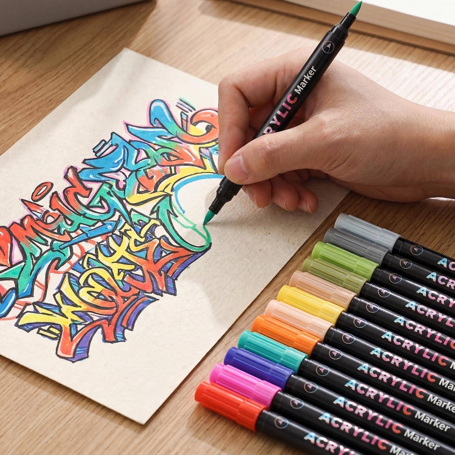 Handgezeichnete bunte Graffiti-ähnliche Beschriftung auf Papier mit einem Acrylmarker, neben einer Reihe verschiedenfarbiger Marker auf einem Holzschreibtisch.