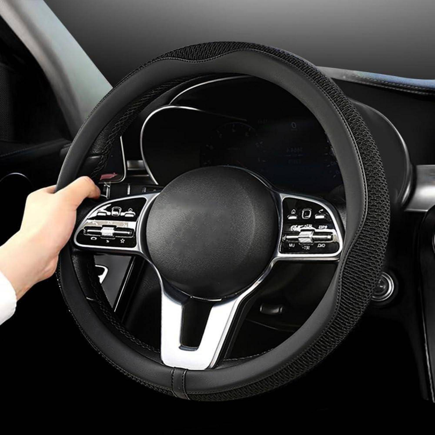 Hand hält einen schwarzen Lenkradschutz mit silbernen Steuertasten in einem Autoinnenraum.