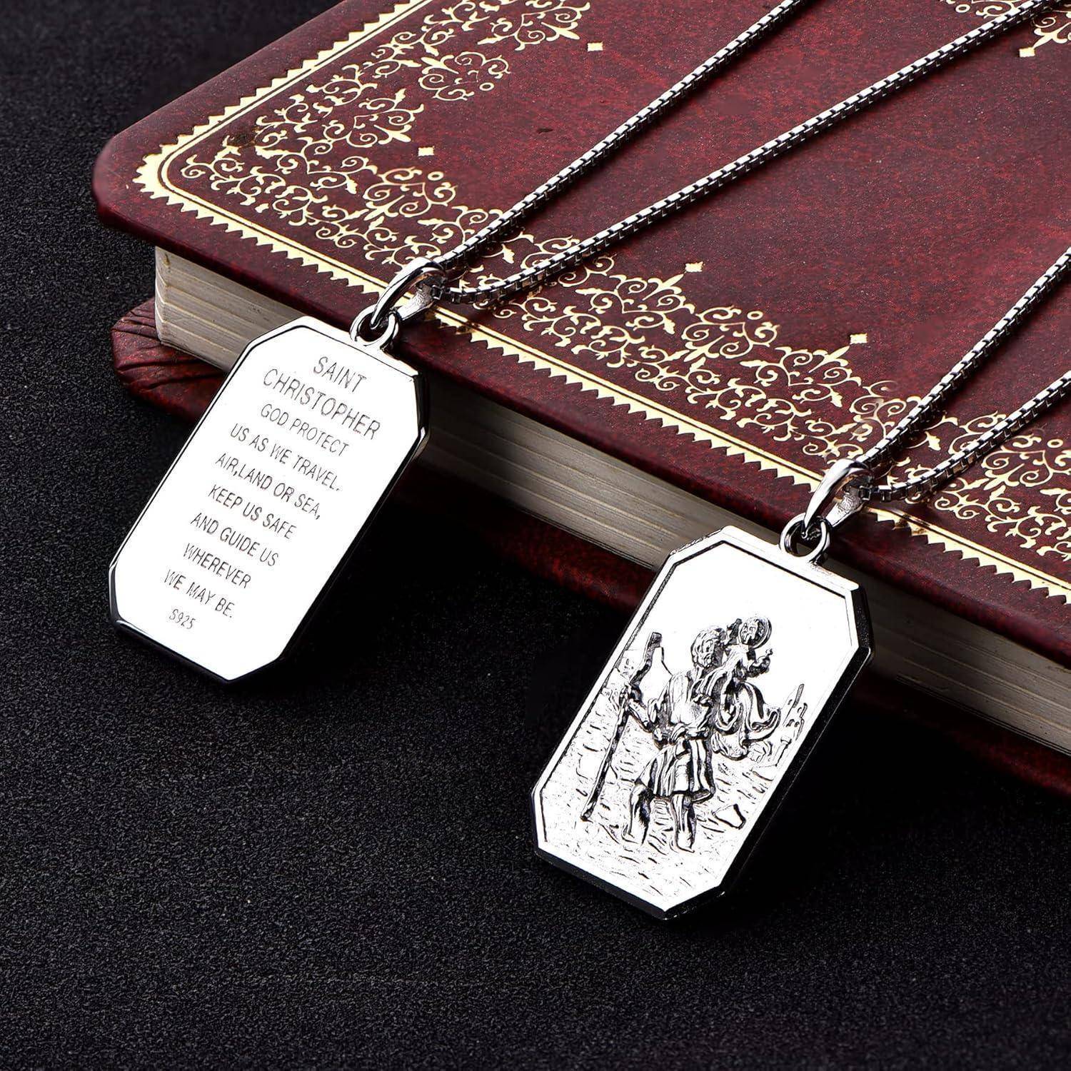 Zwei Saint-Christopher-Halsketten mit gravierten Silberanhängern, die auf einem gemusterten roten Buch ruhen, eine mit einem Gebet und eine mit einem religiösen Bild.
