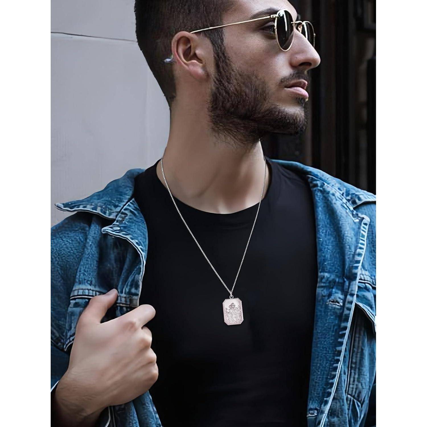 Stilvoller Mann mit Sonnenbrille und Jeansjacke, der eine Anhängerkette trägt und nach draußen blickend.