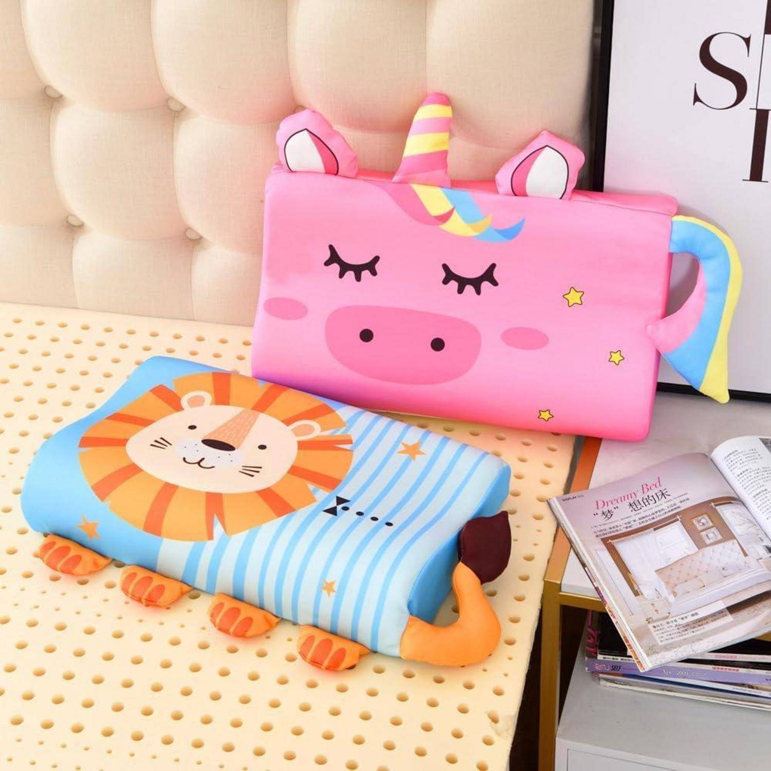 Zwei bunte Plüschkissen für Kinder in Form eines rosa Einhorns und eines blauen Löwen ruhen auf einem Bett und verleihen dem Raum einen verspielten, dekorativen Touch.