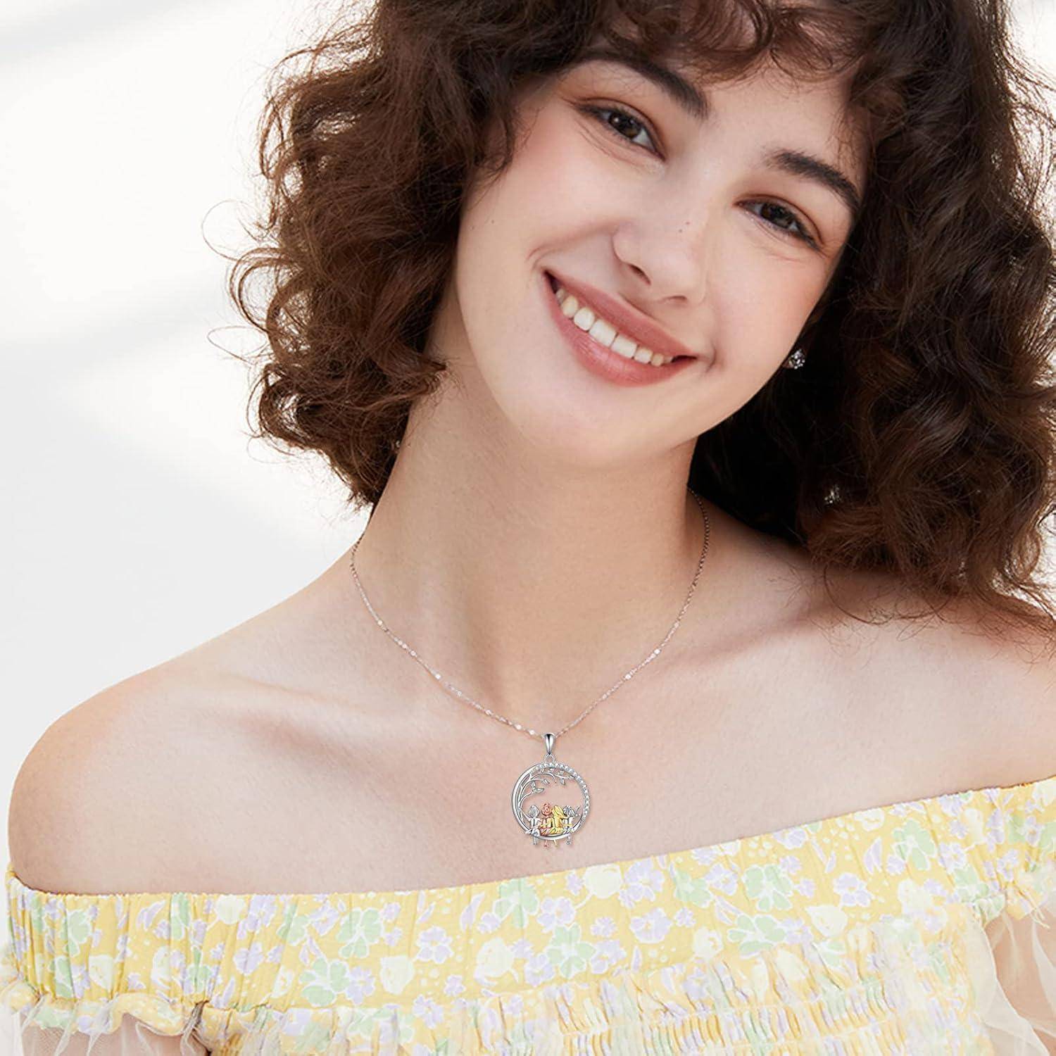 Lächelnde Frau mit lockigem Haar, die ein schulterfreies gelbes Blumenshirt und eine silberne Anhängerkette vor einem weißen Hintergrund trägt.