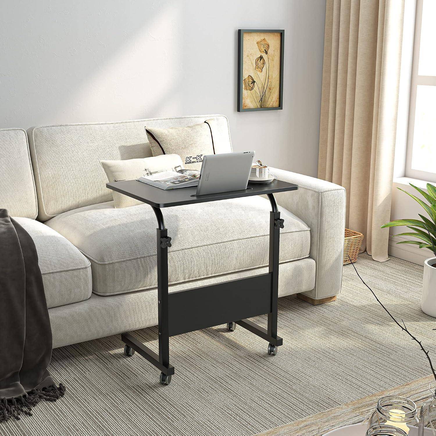 Ein rollbarer Laptop-Tabletttisch steht vor einem hellen Sofa in einem hellen Wohnzimmer, mit einem Laptop und einem Kaffeeservice oben drauf.