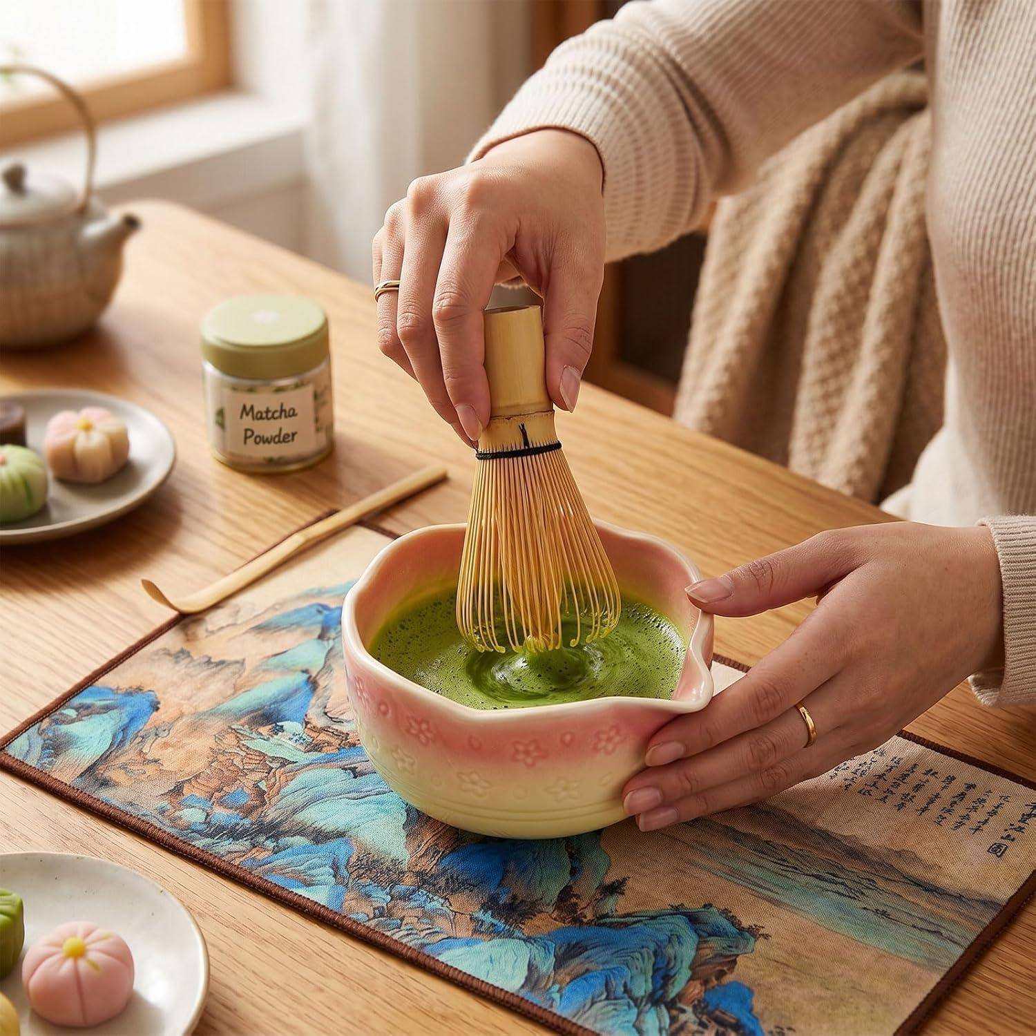 Person, die Matcha in einer rosa Schale auf einem Holztisch aufschlägt, mit einem 