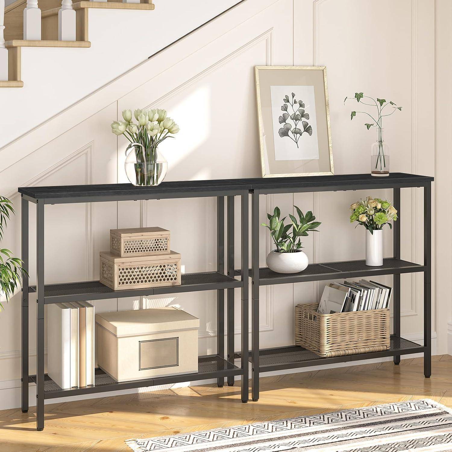Zwei schwarze Konsolentische unter einer Treppe präsentieren Blumen, gerahmte Kunstwerke, Bücher, Boxen und Körbe in einem hellen Eingangsbereich.