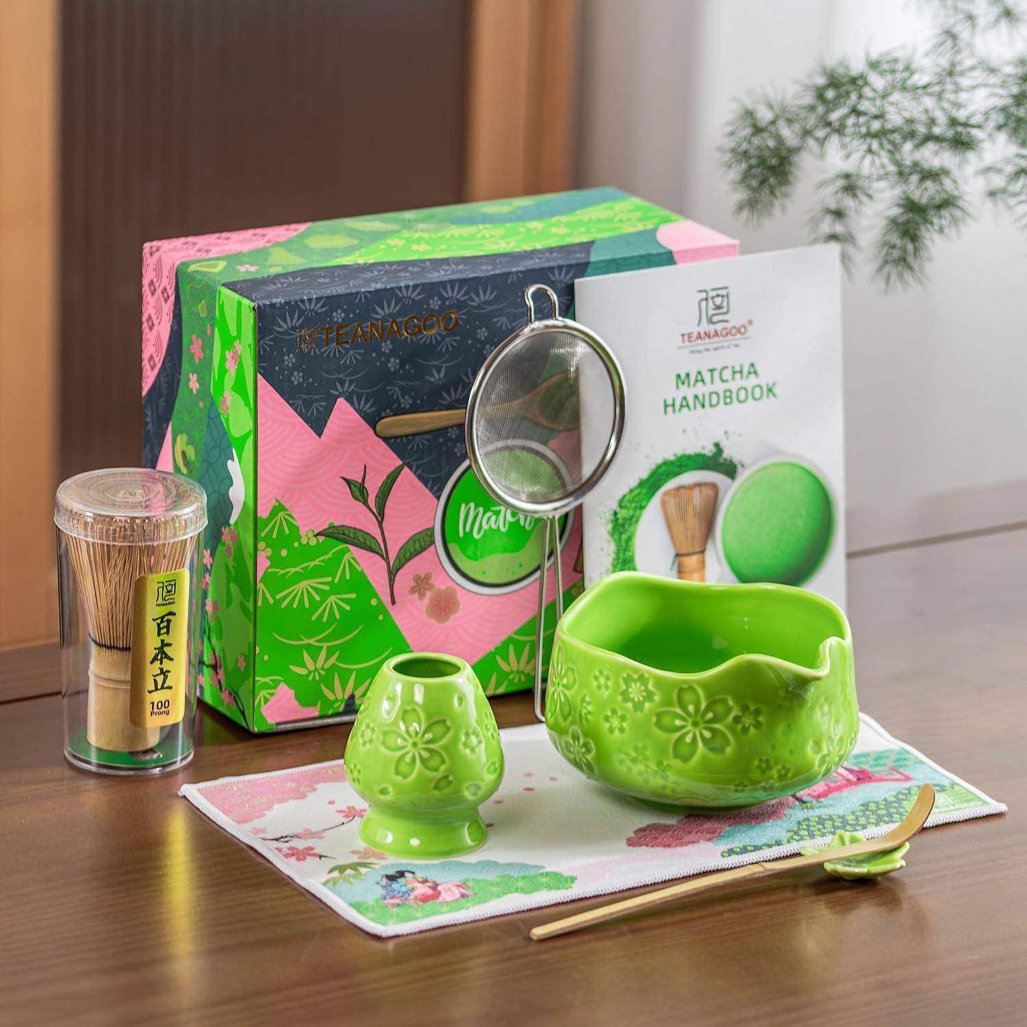 Matcha-Tee-Set auf einem Tisch mit einer grünen Keramikschale und Tasse, Bambusbesenquaste, Matcha-Dose, Sieb, Handbuch und dekorativem Karton.