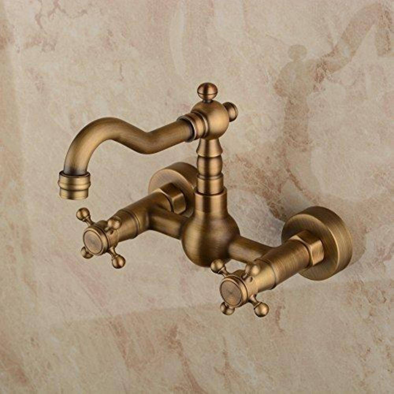 Wandmontierter Messing-Wasserhahn im Antik-Stil mit Kreuzhebeln und geschwungenem Auslauf an einer Stein- oder Marmorwand.