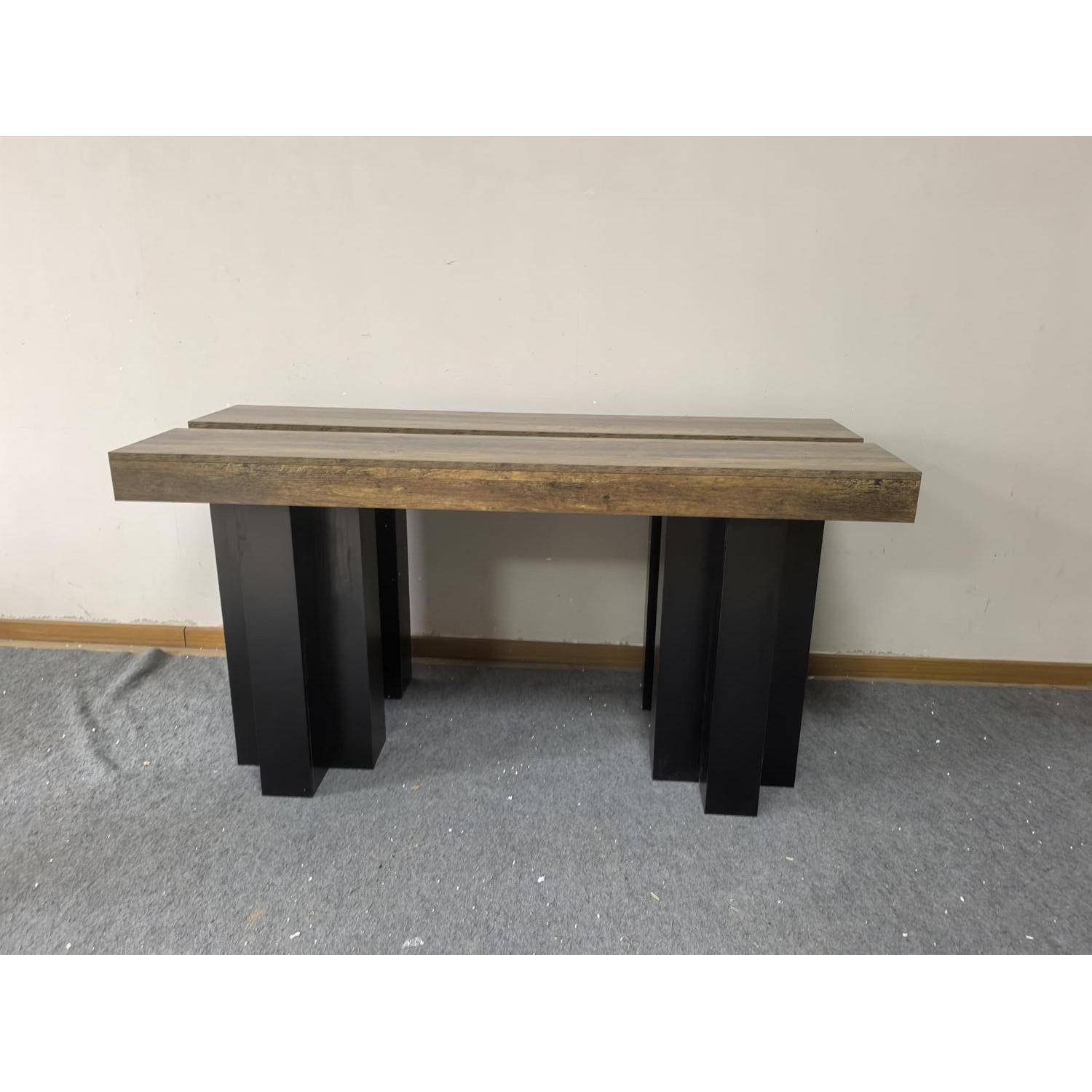 Ein moderner rechteckiger Holztisch mit einer dicken Platte und vier schwarzen blockartigen Beinen, vor einer schlichten Wand auf einem Teppich dargestellt.