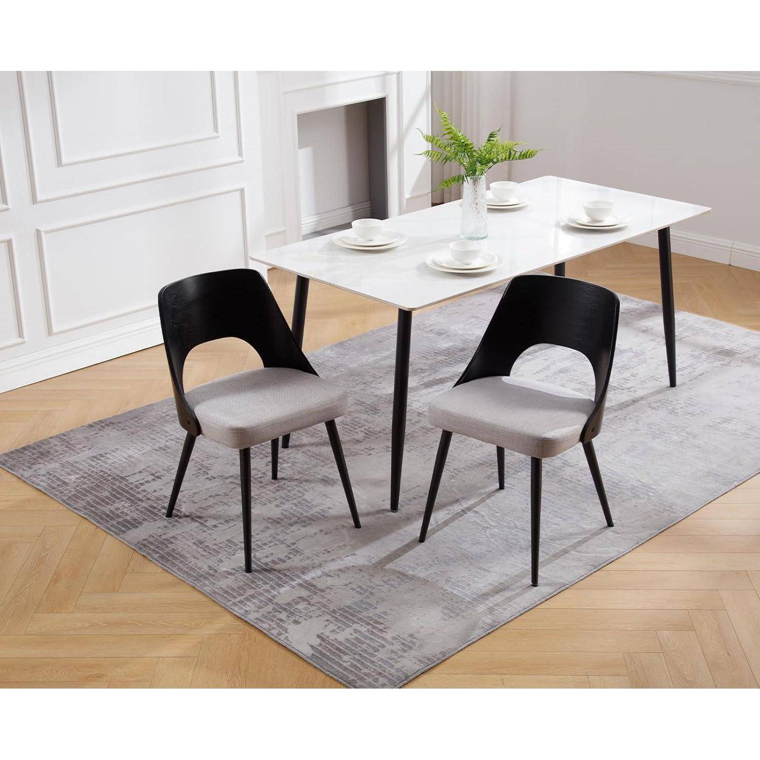 Zwei schwarz-graue Esszimmerstühle um einen weißen Tisch mit Tellern, auf einem grauen Teppich in einem hellen Raum.