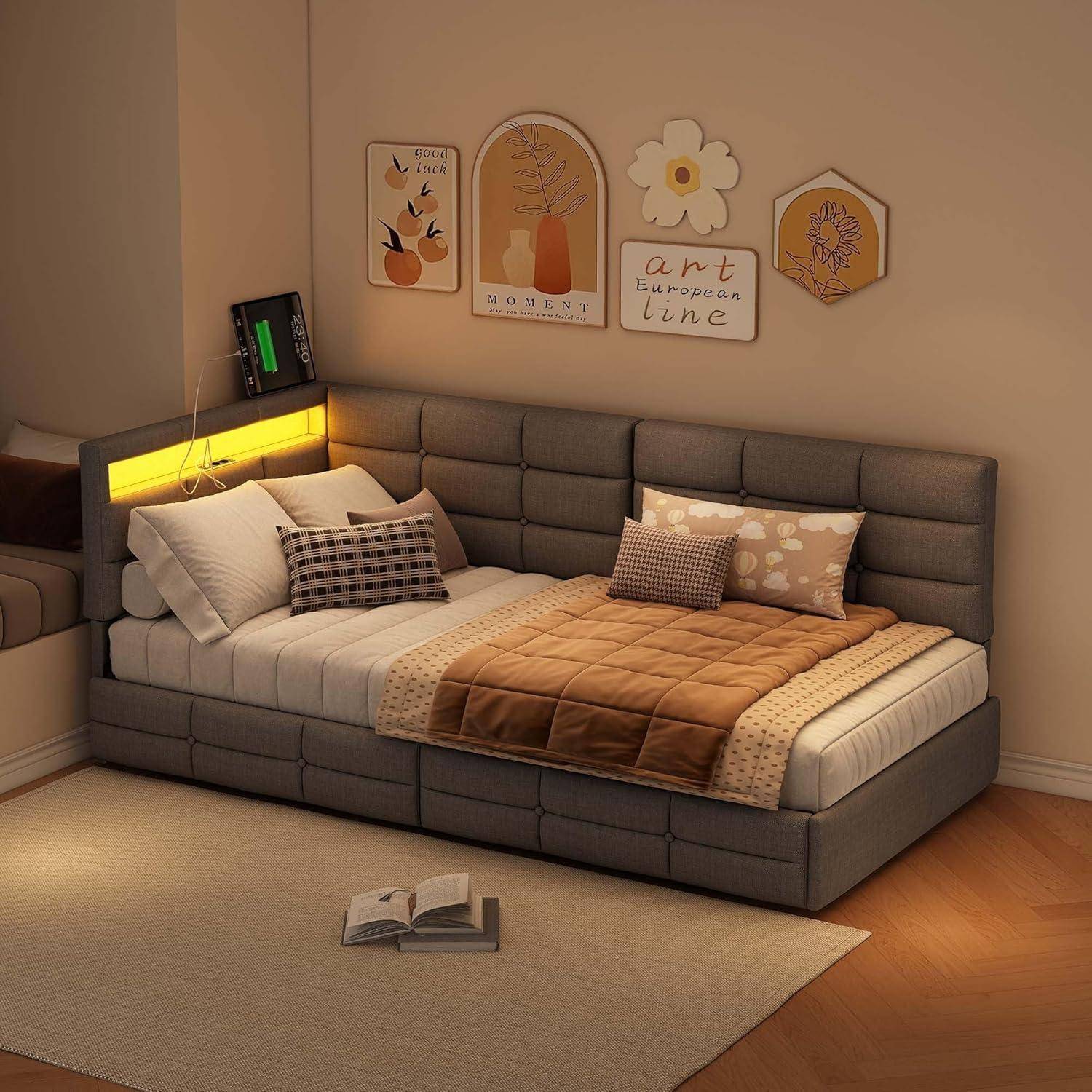 Modernes Schlafzimmer mit einem grau gepolsterten Bett, warm hinterleuchtetem Kopfteil und Kunstdrucken darüber; ein aufgeschlagenes Buch liegt auf dem Teppich.
