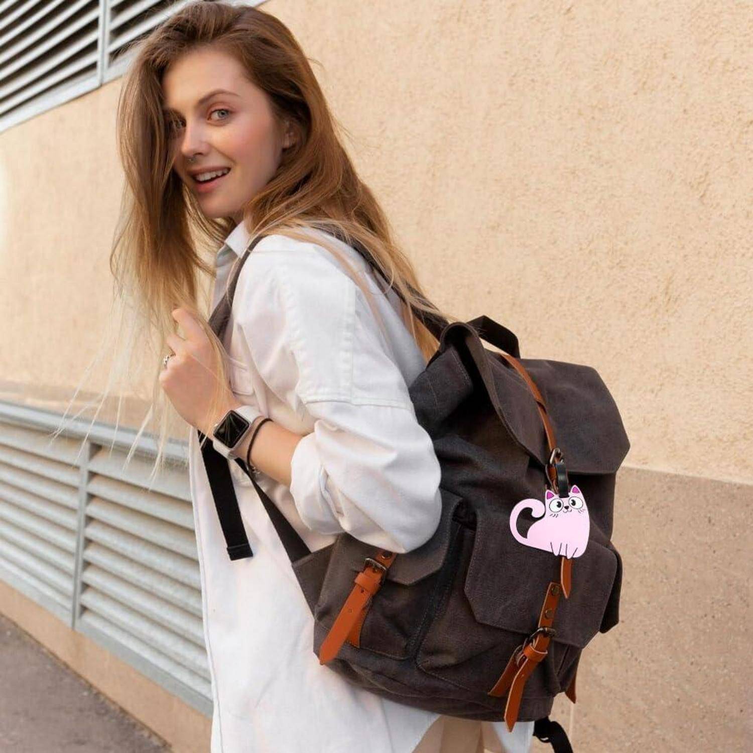 Junge Frau, die im Freien spaziert, mit einem Lächeln im weißen Hemd und einem schwarzen Rucksack mit einem rosafarbenen Katzenschmuck.