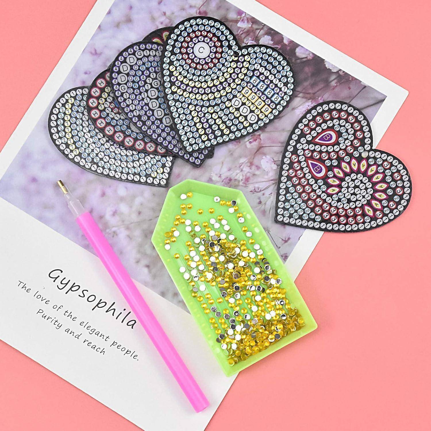 Diamond-Painting-Bastelset mit drei herzförmigen Designs und einem grünen Edelsteintablett auf einer „Gypsophila"-Verpackung mit einem rosa Stift-Pen
