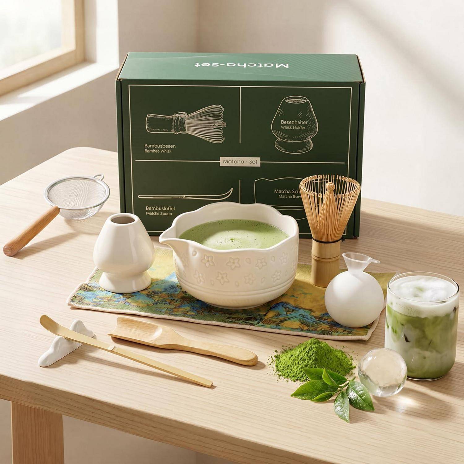 Matcha-Tee-Set auf einem Holztisch, einschließlich Schüssel, Schneebesen, Sieb, Löffel, Bambushalter, Matcha-Pulver und gekühltem Matcha-Getränk in einer Produktpräsentation.