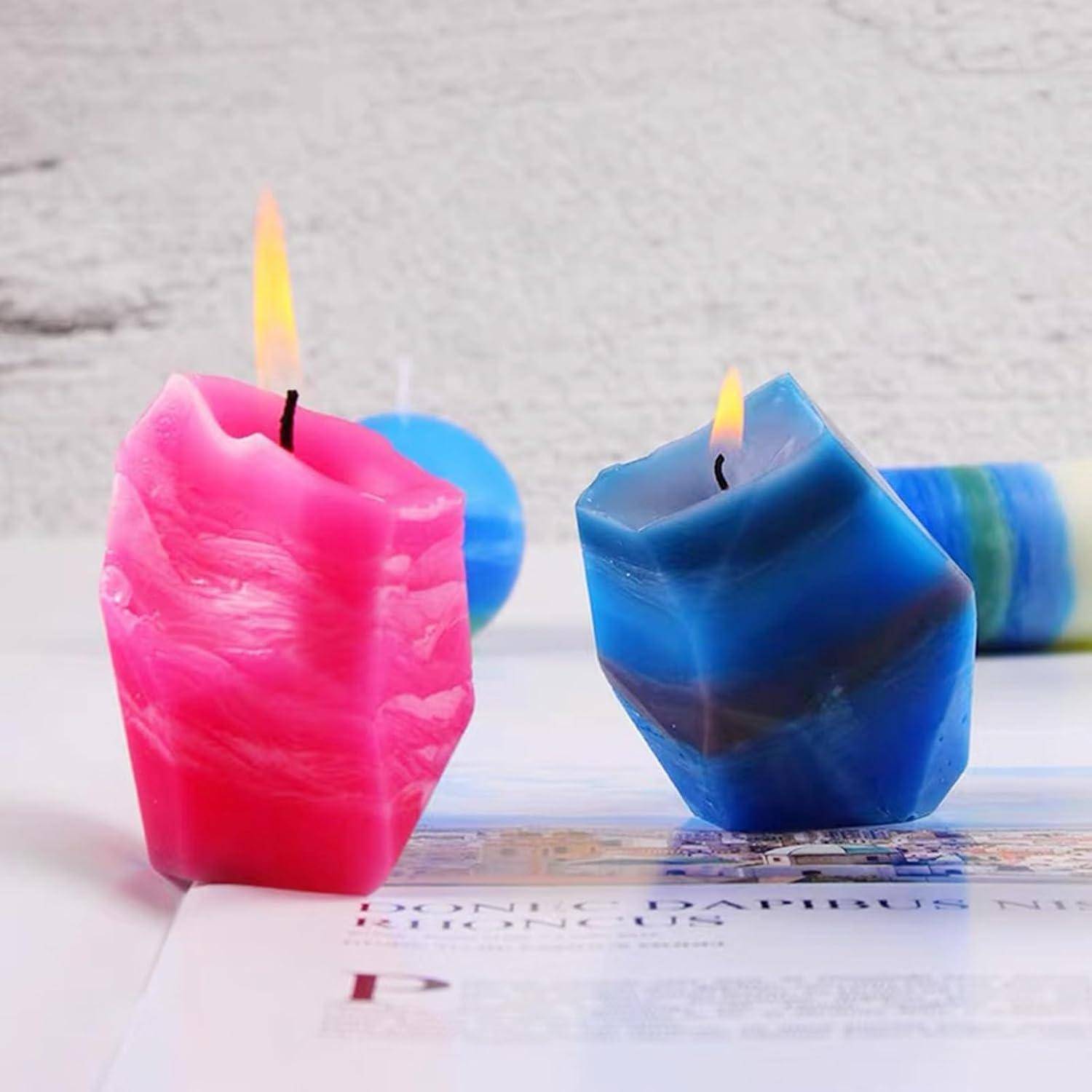 Zwei brennende dekorative Kerzen, eine rosa und eine blaue, stehen auf einer Zeitschriftenseite vor einer hellen Wand.