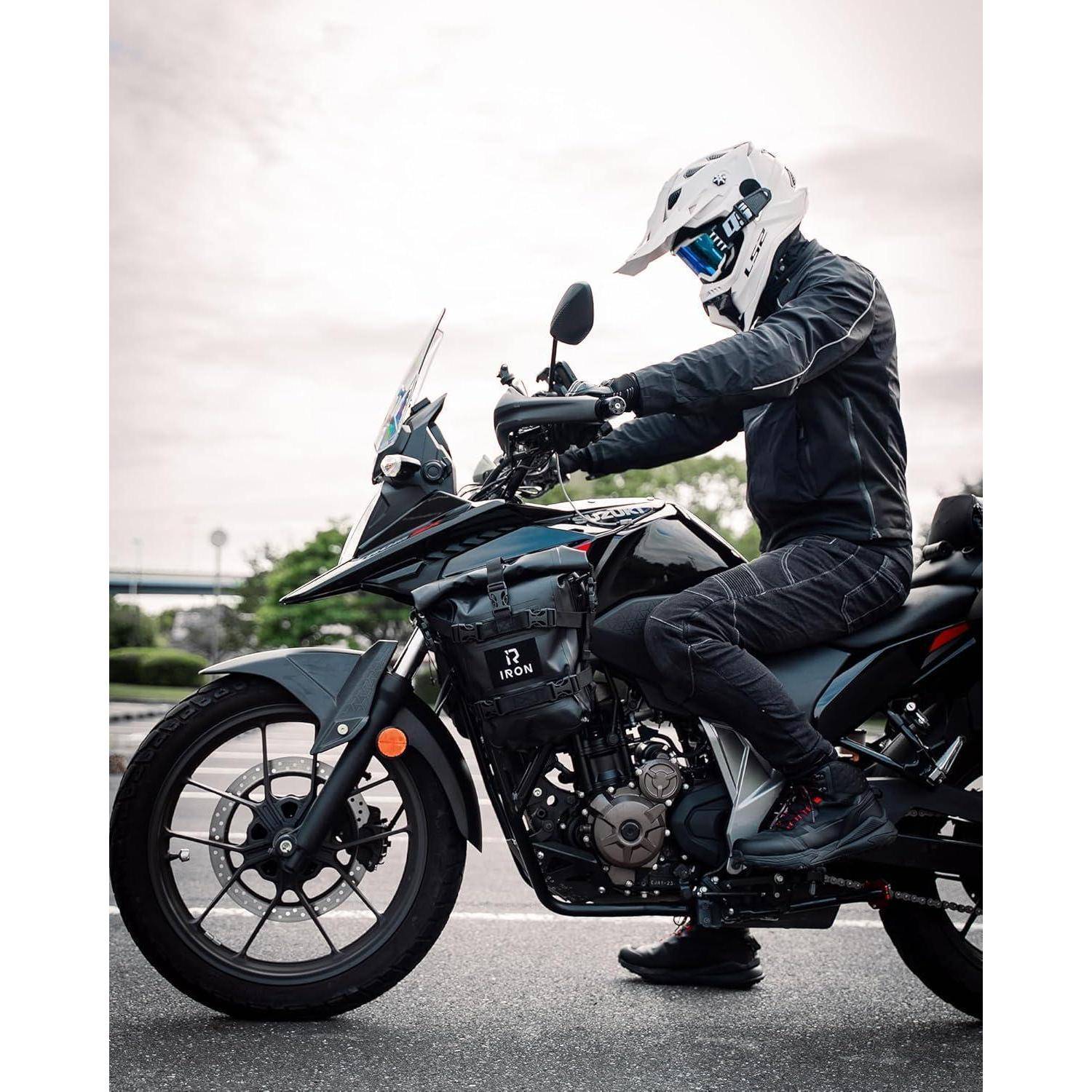 Motorradfahrer in schwarzer Ausrüstung und weißem Helm, der ein schwarzes Adventure-Motorrad auf einer Straße fährt.