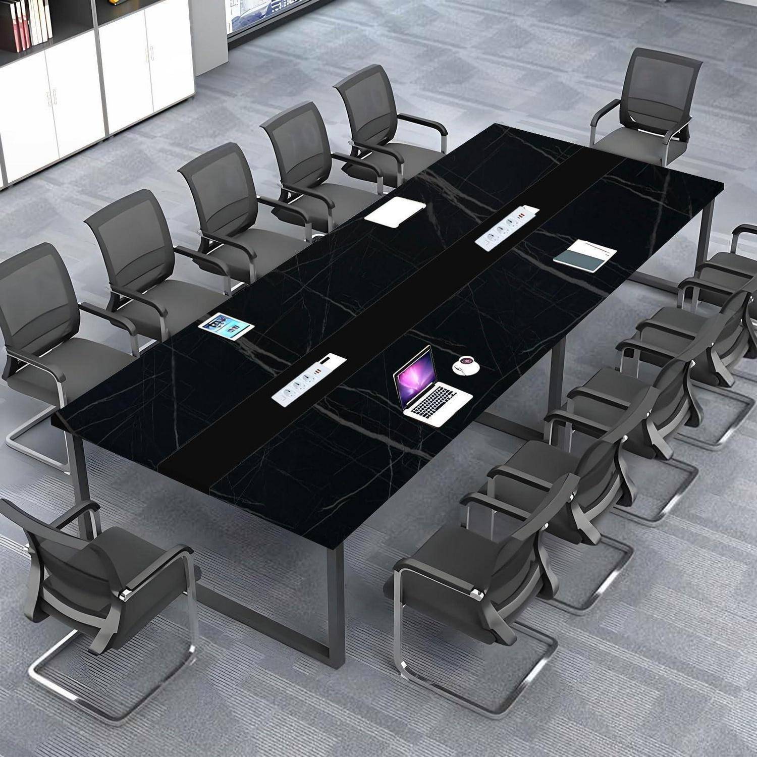 Leerer Konferenzraum mit einem großen schwarzen Konferenztisch, umgeben von vielen Stühlen, auf dem Tisch ein Laptop und einige Dokumente.