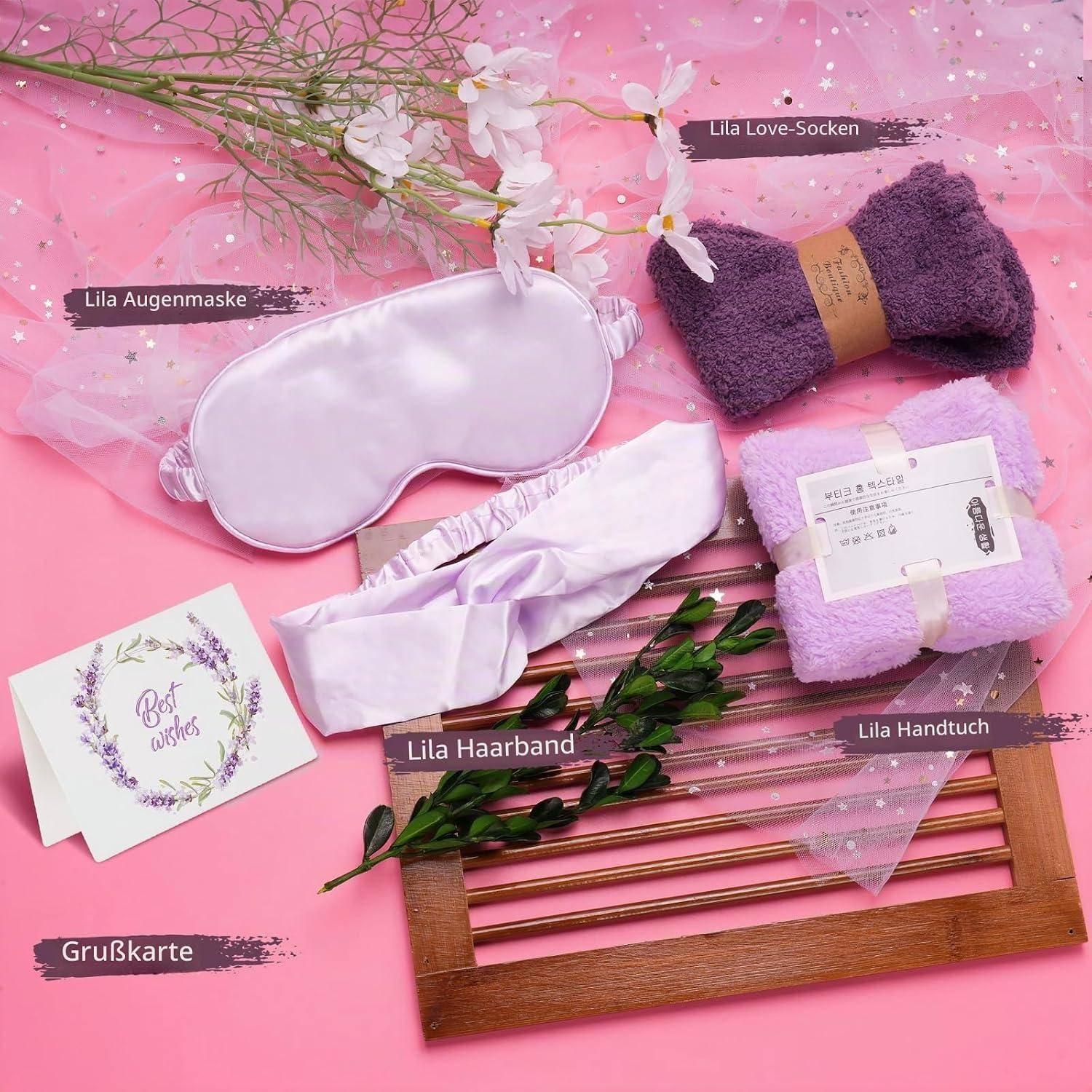 Gemischtes Lavendelgeschenkset auf rosa Hintergrund: Schlafmaske, Socken, Haarband, Handtuch und Grußkarte mit Etiketten auf Deutsch.