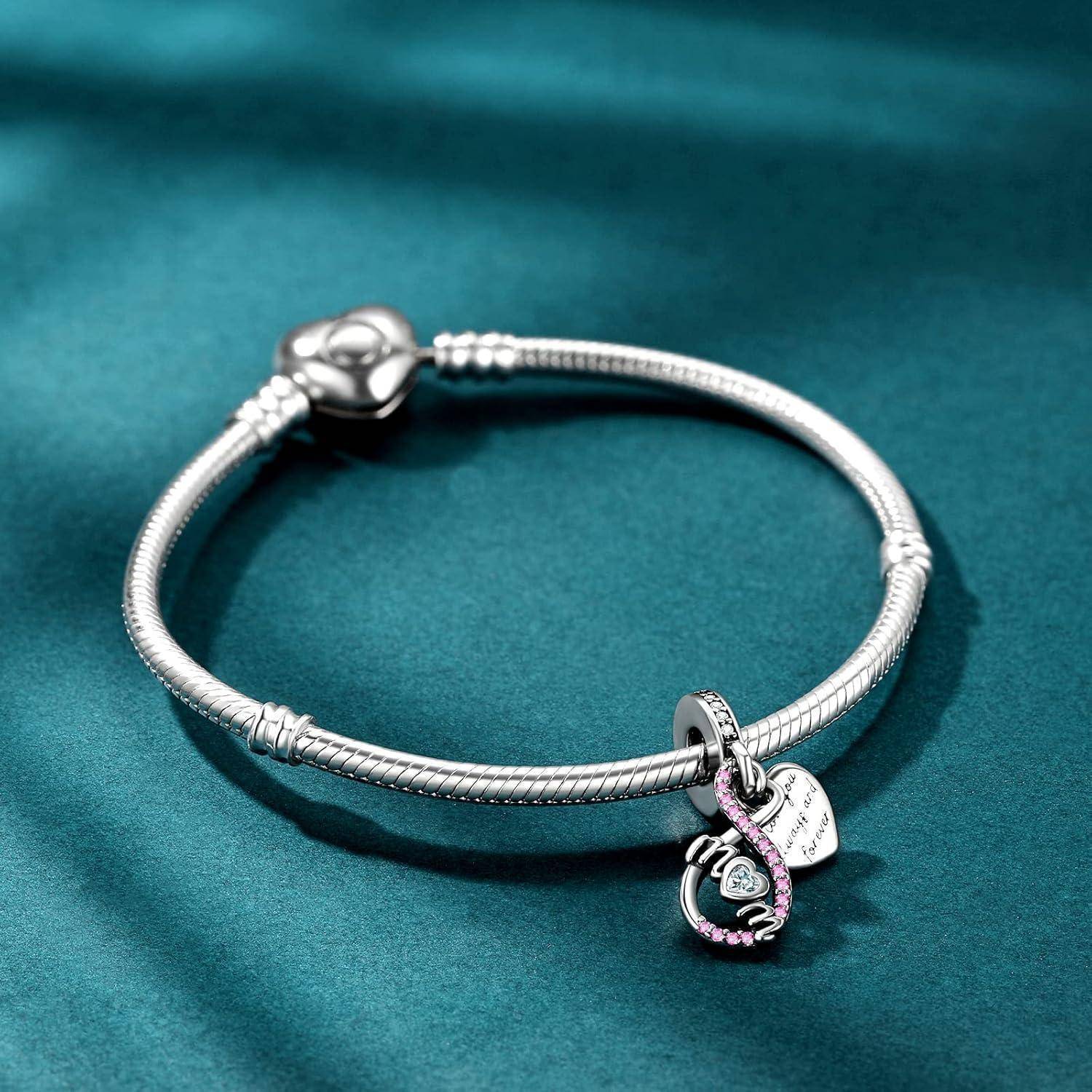 Silberarmband mit rundem Verschluss und drei baumelnden Anhängern, darunter ein rosa verziertes Herz und ein 