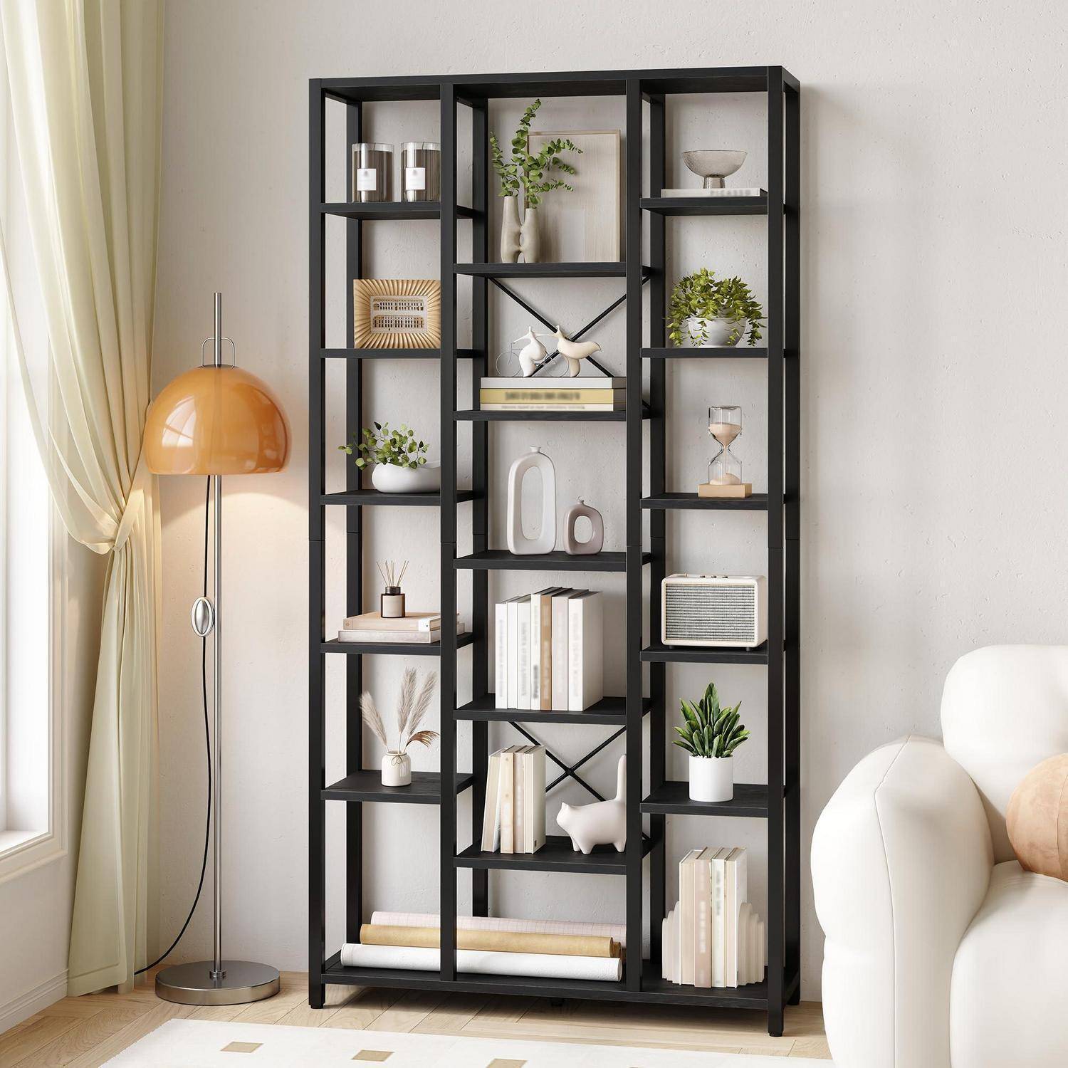 Hohes schwarzes Metallregal mit Büchern, Pflanzen, Dekorationselementen und Aufbewahrungsgegenständen neben einer bernsteinfarbenen Stehleuchte in einem modernen Wohnzimmer.